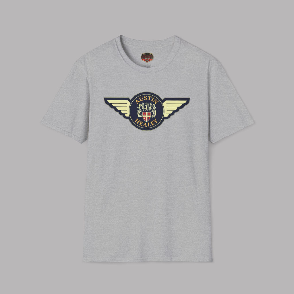 Austin Healey winged badge logo with navy and gold circular emblem, heraldic shield, and cream wings on a sport gray t-shirt flat on gray background