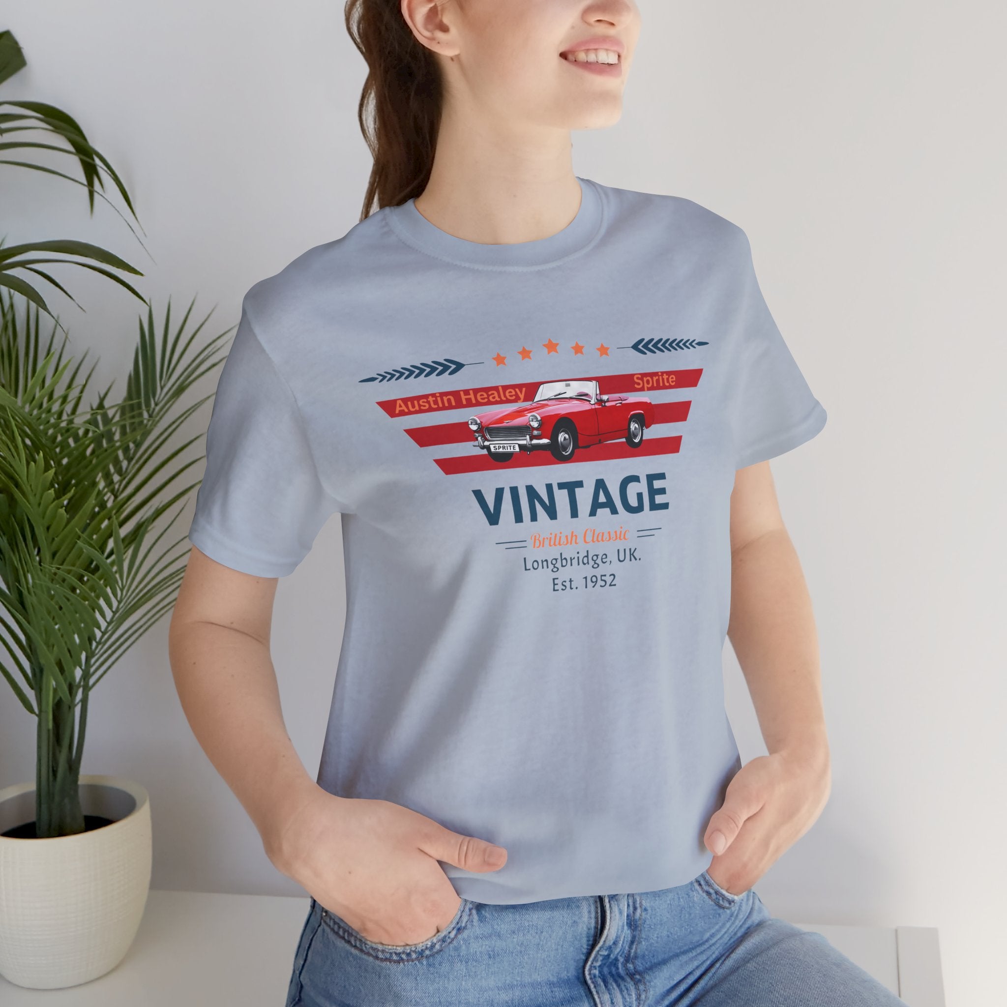 Woman wearing a light blue t-shirt with a vintage car design, standing indoors next to a plant.