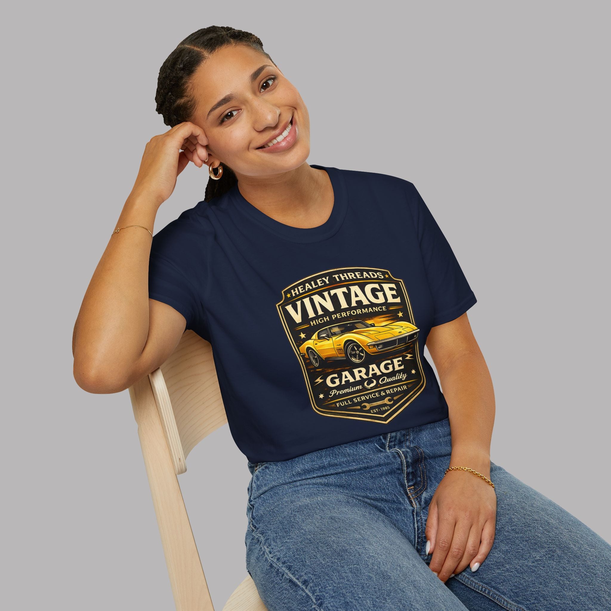 Woman wearing a navy blue t-shirt with a vintage classic car graphic, sitting on a chair against a gray background.