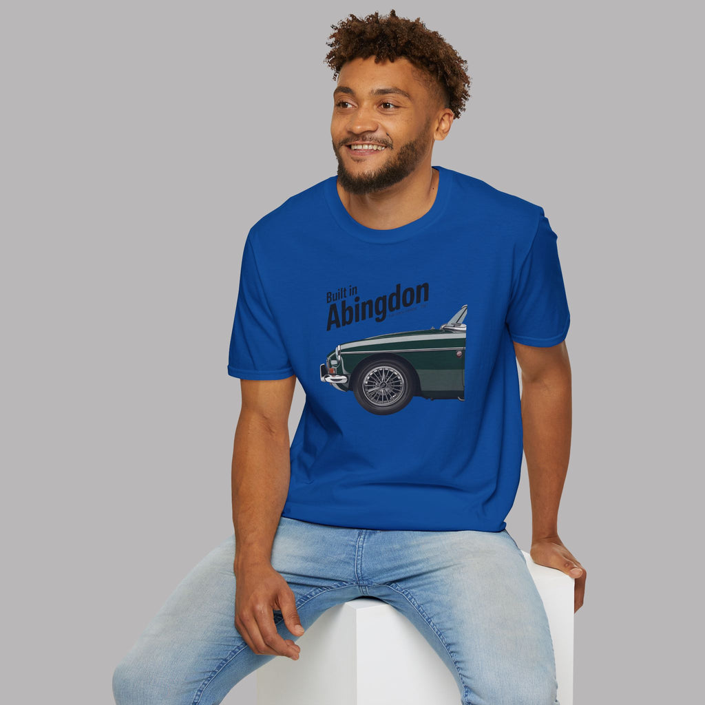 Man wearing a royal blue t-shirt with a classic car graphic and text, sitting on a white stool against a gray background