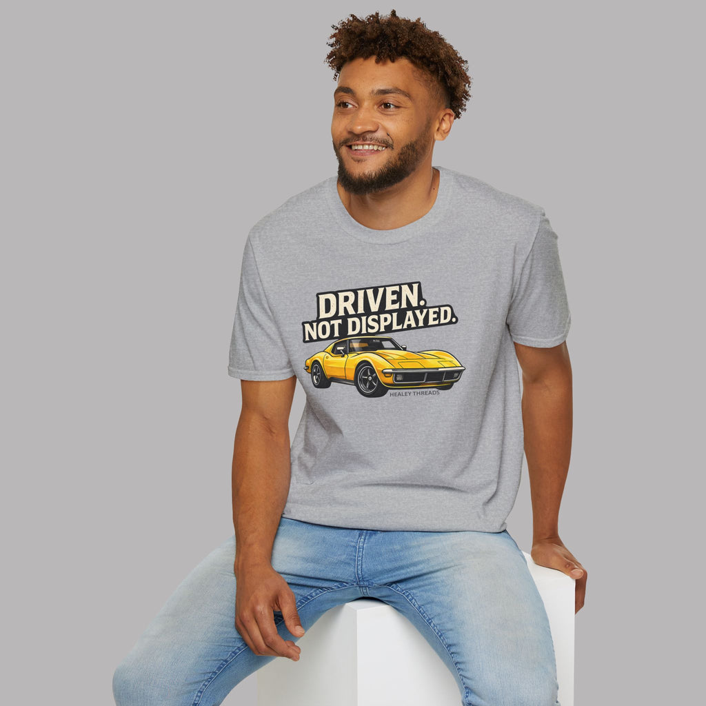 Man wearing a sport gray t-shirt with a muscle car graphic and text, sitting on a white stool against a gray background.