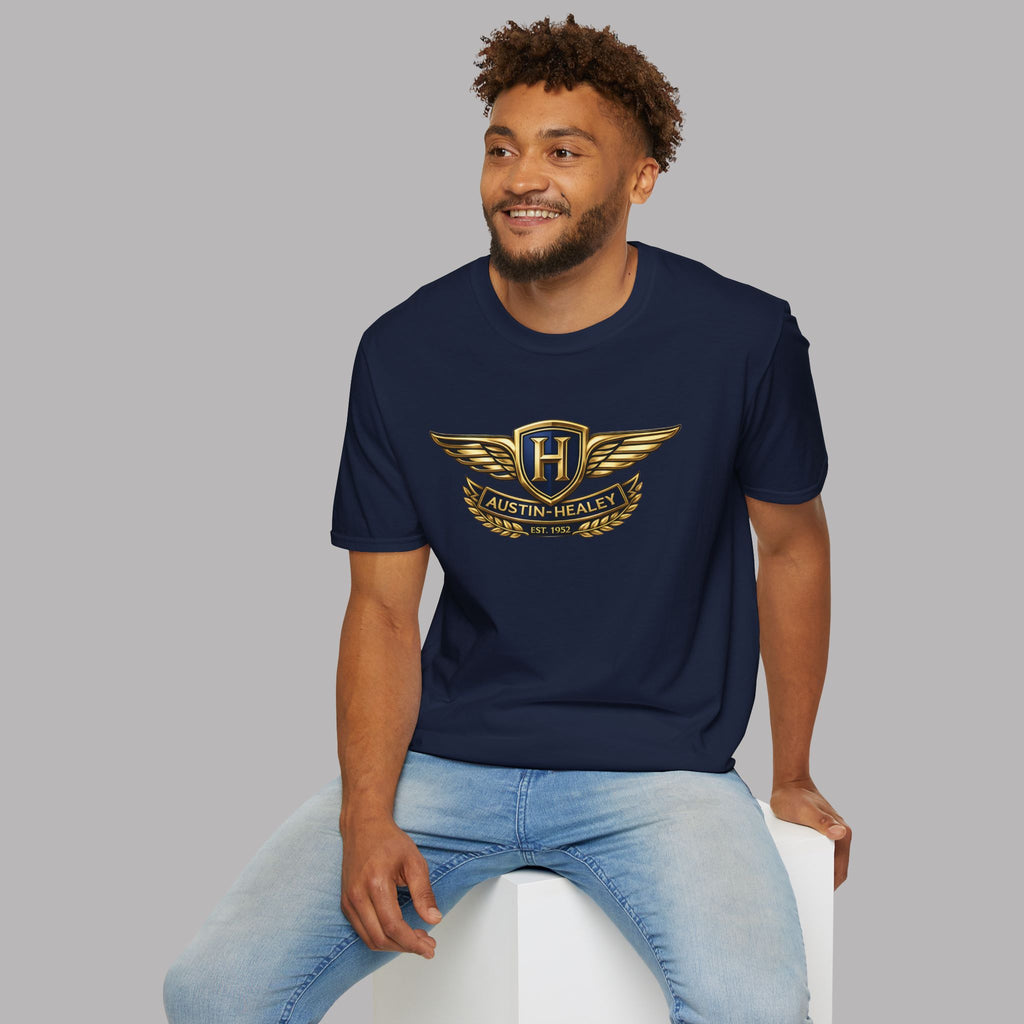 Man wearing a navy blue t-shirt with a gold Healey logo sitting on a white stool against a gray background