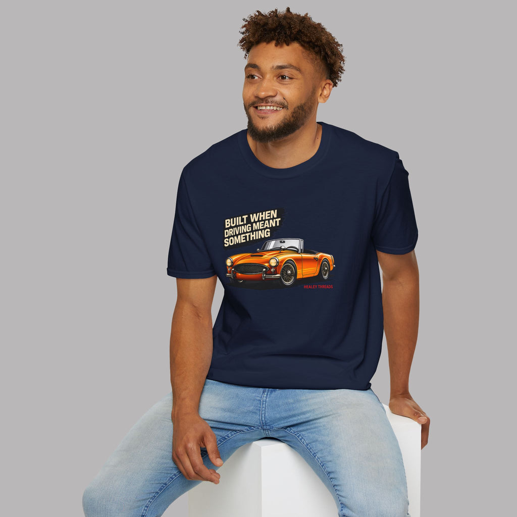 Man wearing a navy blue t-shirt with a graphic and text, sitting on a white stool against a gray background.