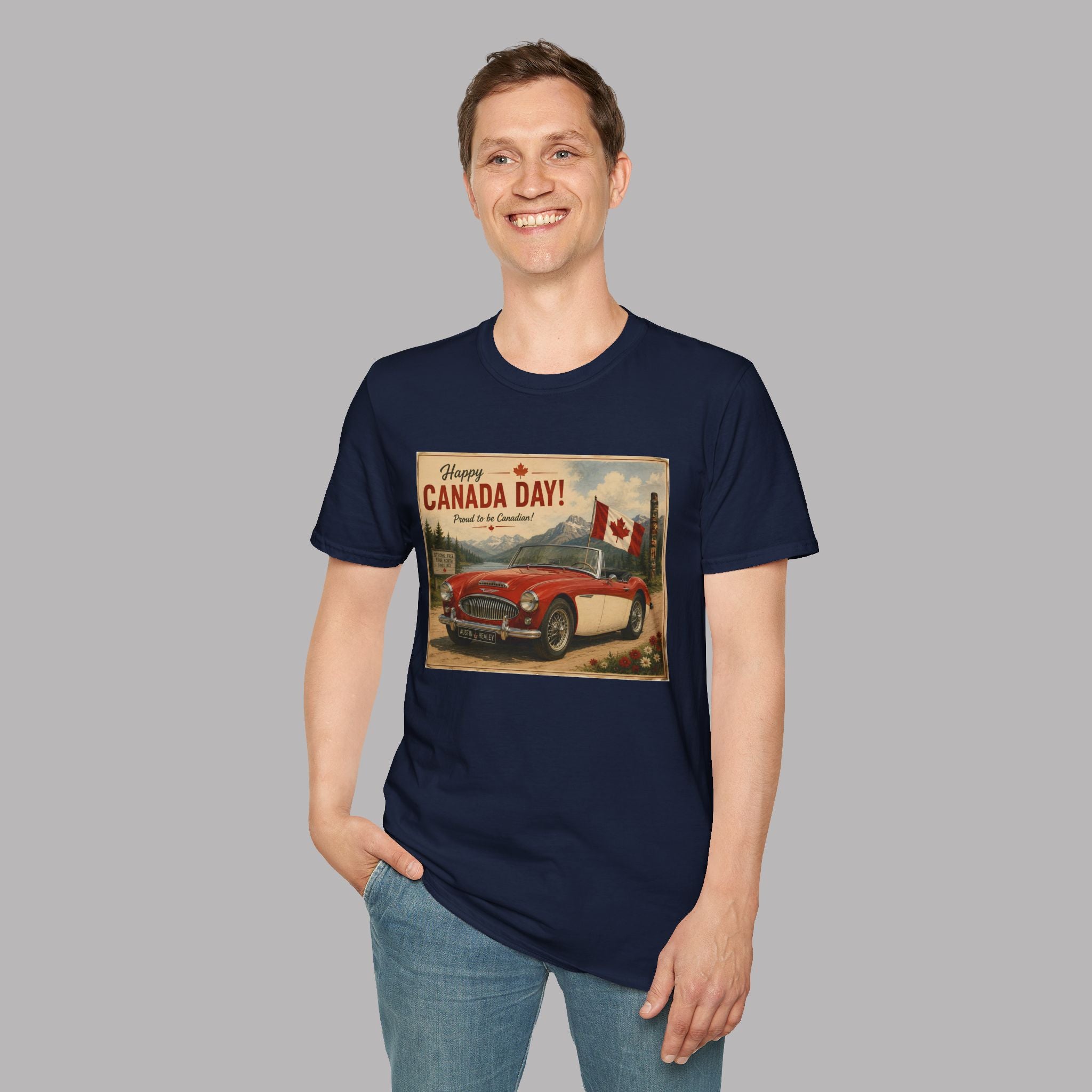 A man wearing a navy blue t-shirt with a vintage-style 'Canada Day!' graphic print featuring a red car and Canadian flags, paired with blue jeans, set against a solid gray background.