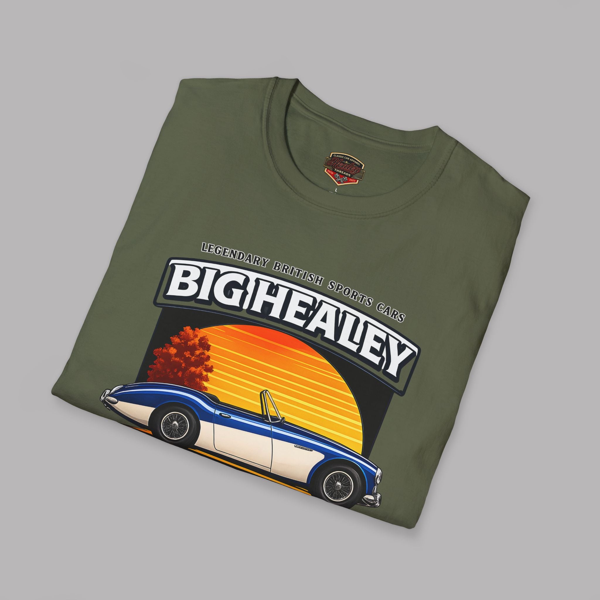 Folded Big Healey graphic military green colored t-shirt featuring a blue and white Austin Healey roadster with retro sunset artwork and vintage British sports car on a gray background