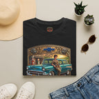 A folded black short-sleeve crewneck t-shirt featuring a vintage-style graphic print of a teal 1957 Chevrolet station wagon with a woman sitting on it, framed by a gold and brown border with the text 'CHEVY QUEEN', on a white background.