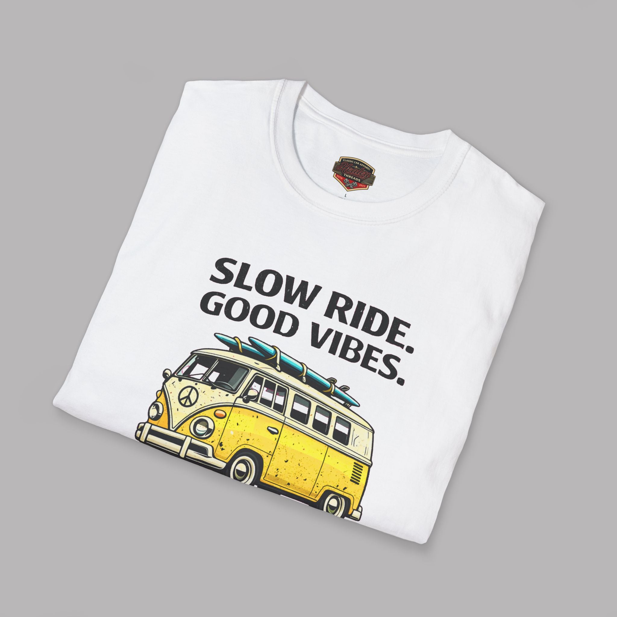 Folded white t-shirt with a yellow van graphic and text 'Slow Ride. Good Vibes.' on a gray background