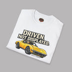 White t-shirt with a yellow muscle car graphic and text 'Driven. Not Displayed.' on a gray background