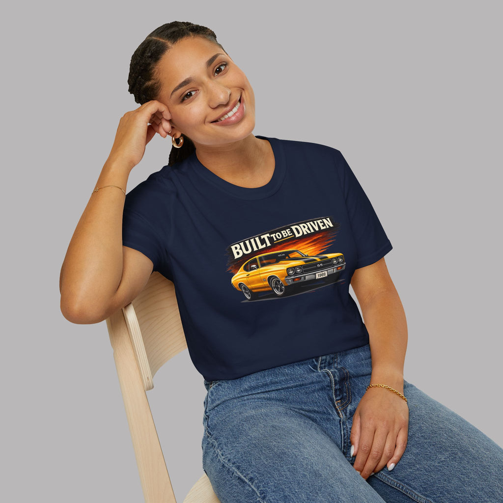 Woman wearing a navy blue t-shirt with a graphic car design and text, sitting on a chair against a gray background.