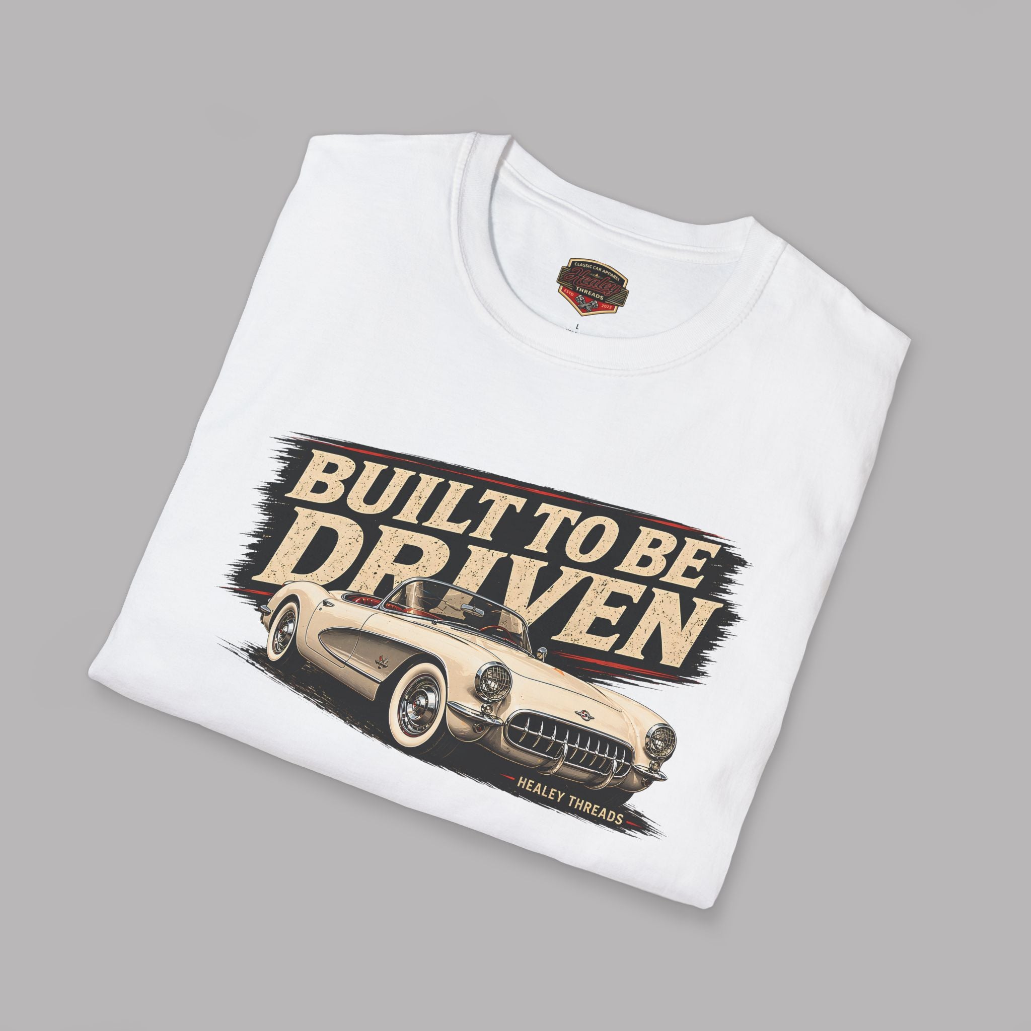 Folded white t-shirt with a graphic of a classic car and 'Built to be Driven' text on a gray background