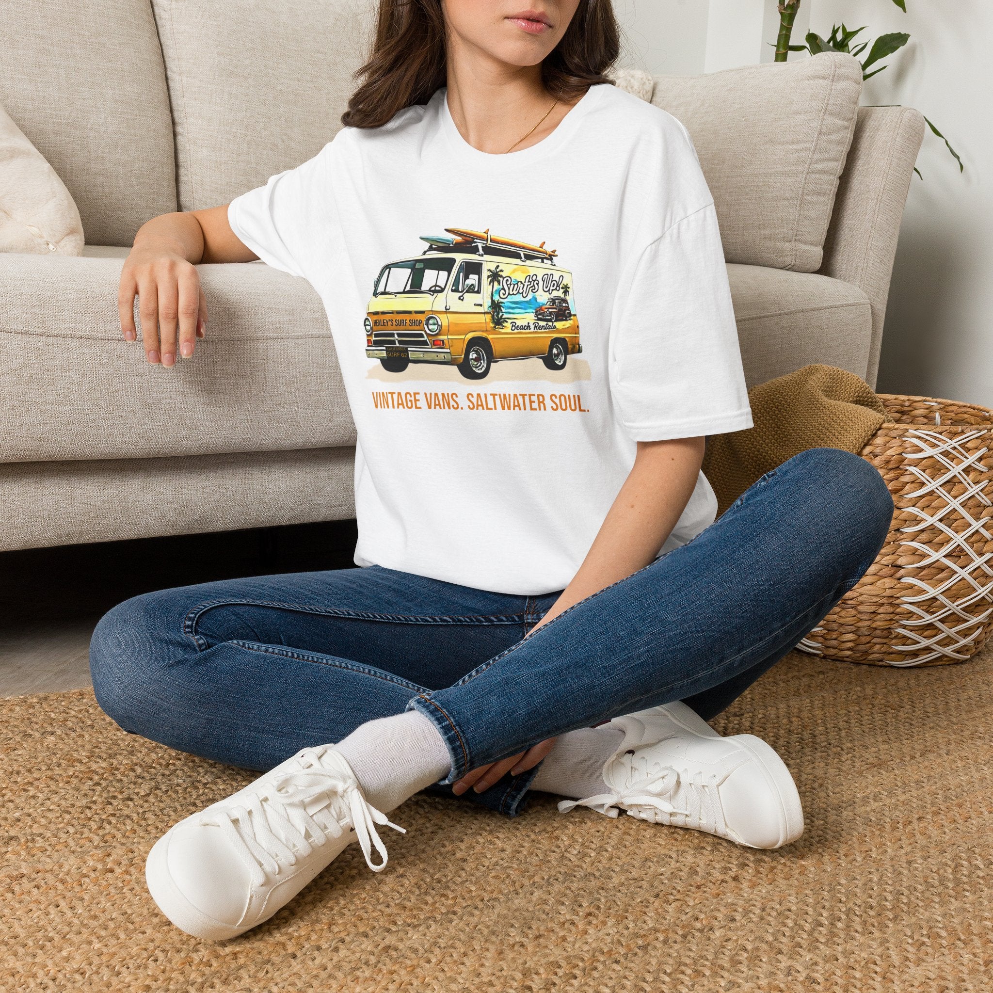 Girl wearing a white t-shirt with text and a vintage van graphic, sitting on the floor in a living room.