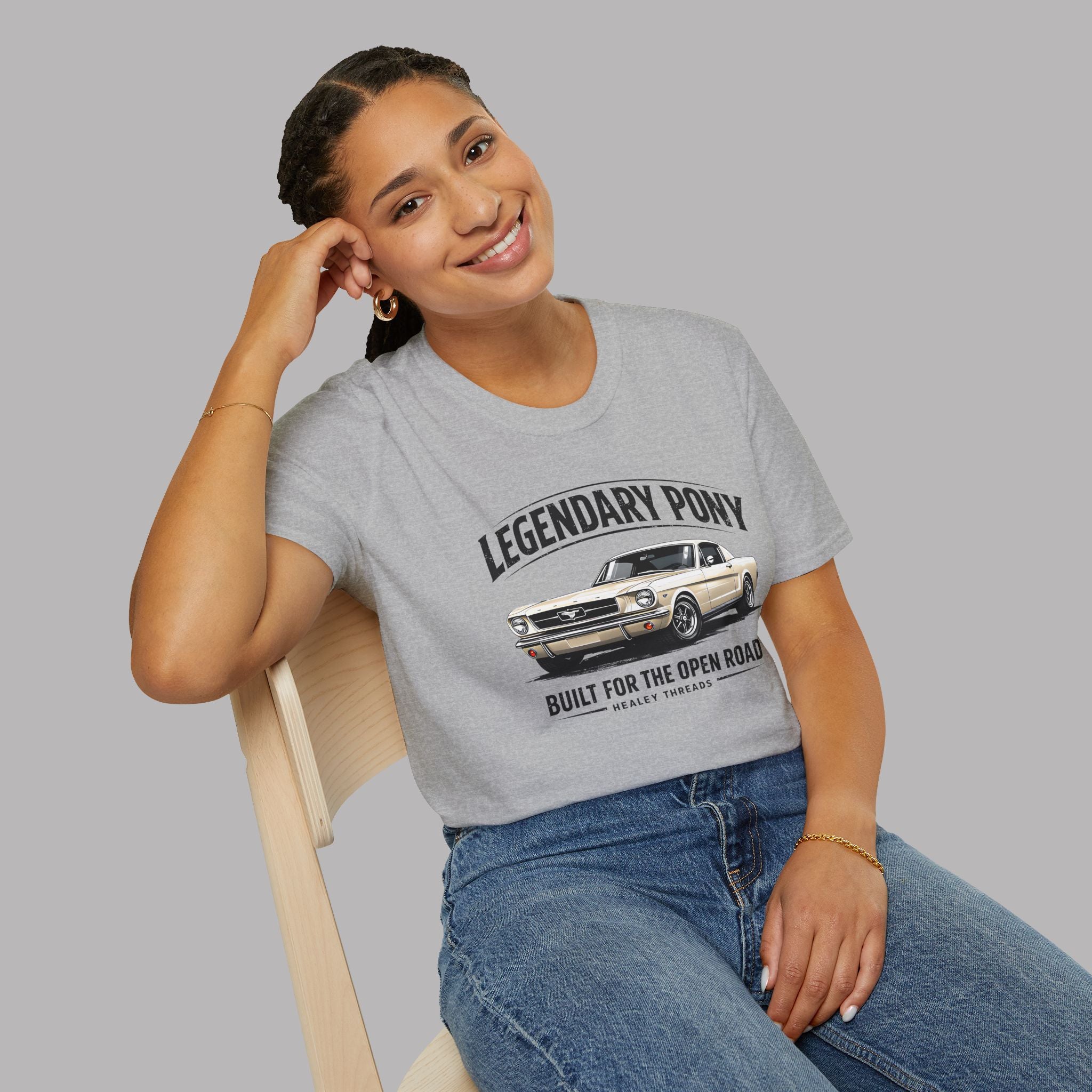 Woman wearing a gray t-shirt with a classic car graphic and text, sitting on a chair against a plain background