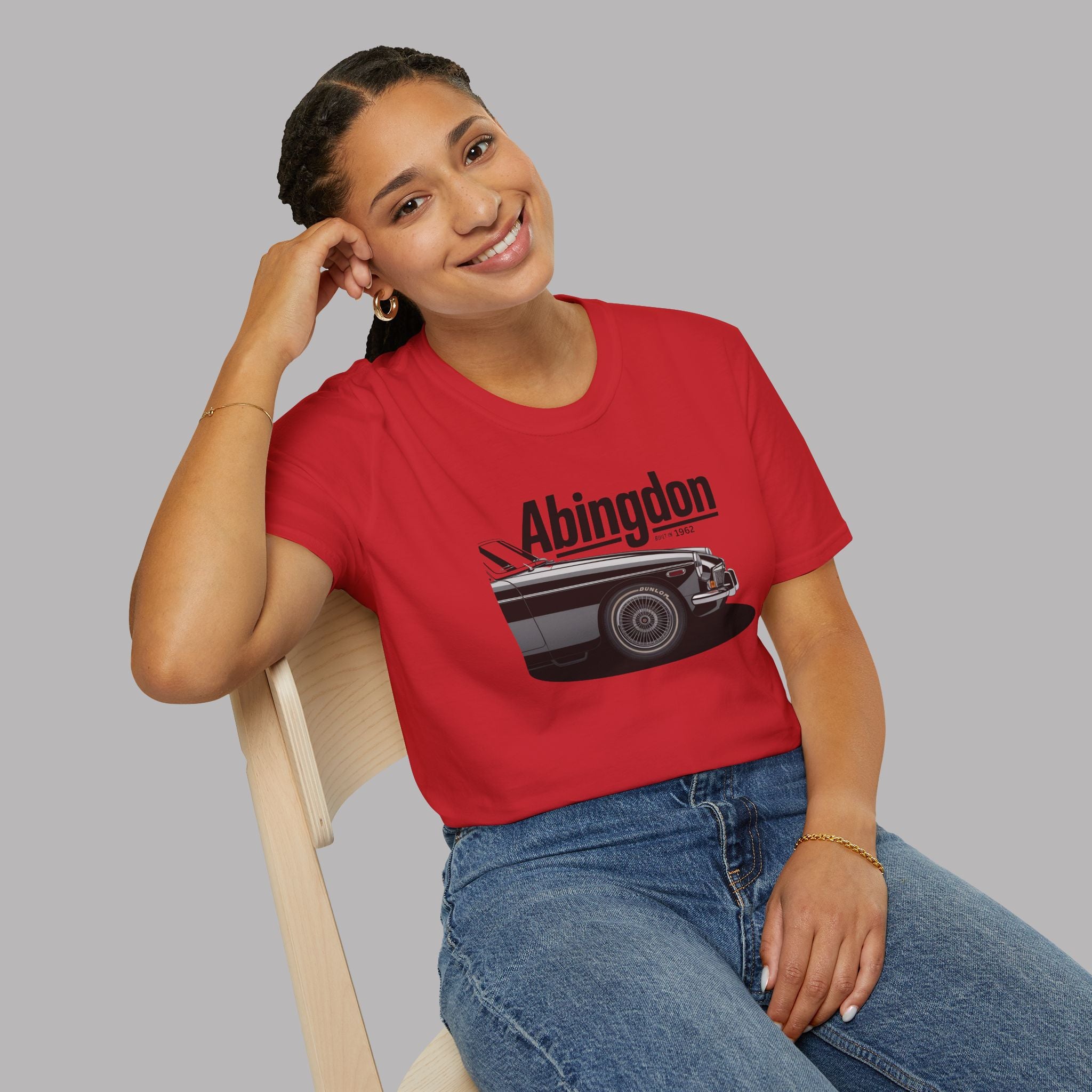 Woman wearing a red t-shirt with a classic car graphic design and text, sitting on a chair against a plain background.