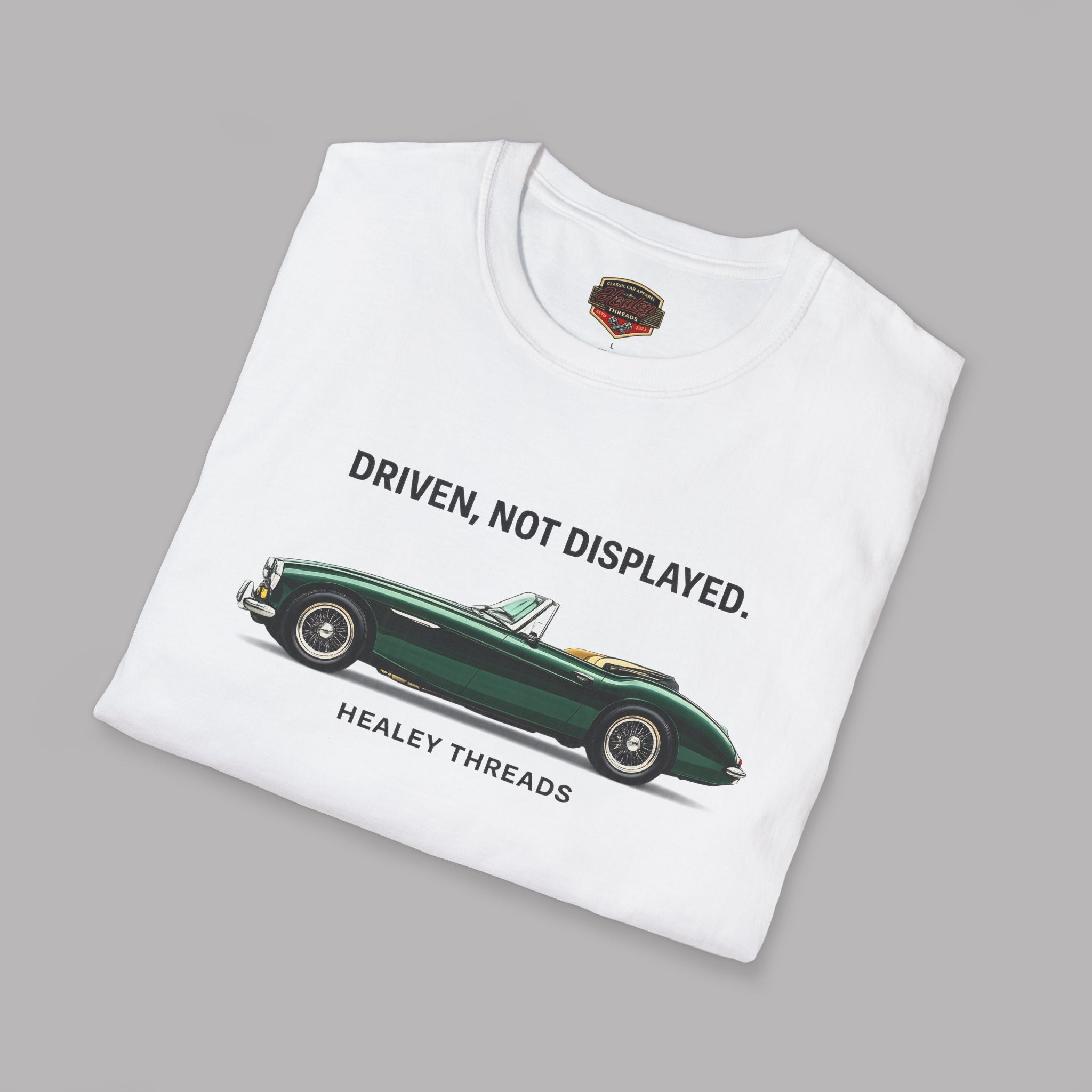 Folded white t-shirt with green classic car graphic and text on a gray background