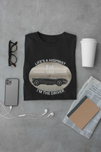 Black t-shirt with vintage car graphic and text on a gray surface with accessories.