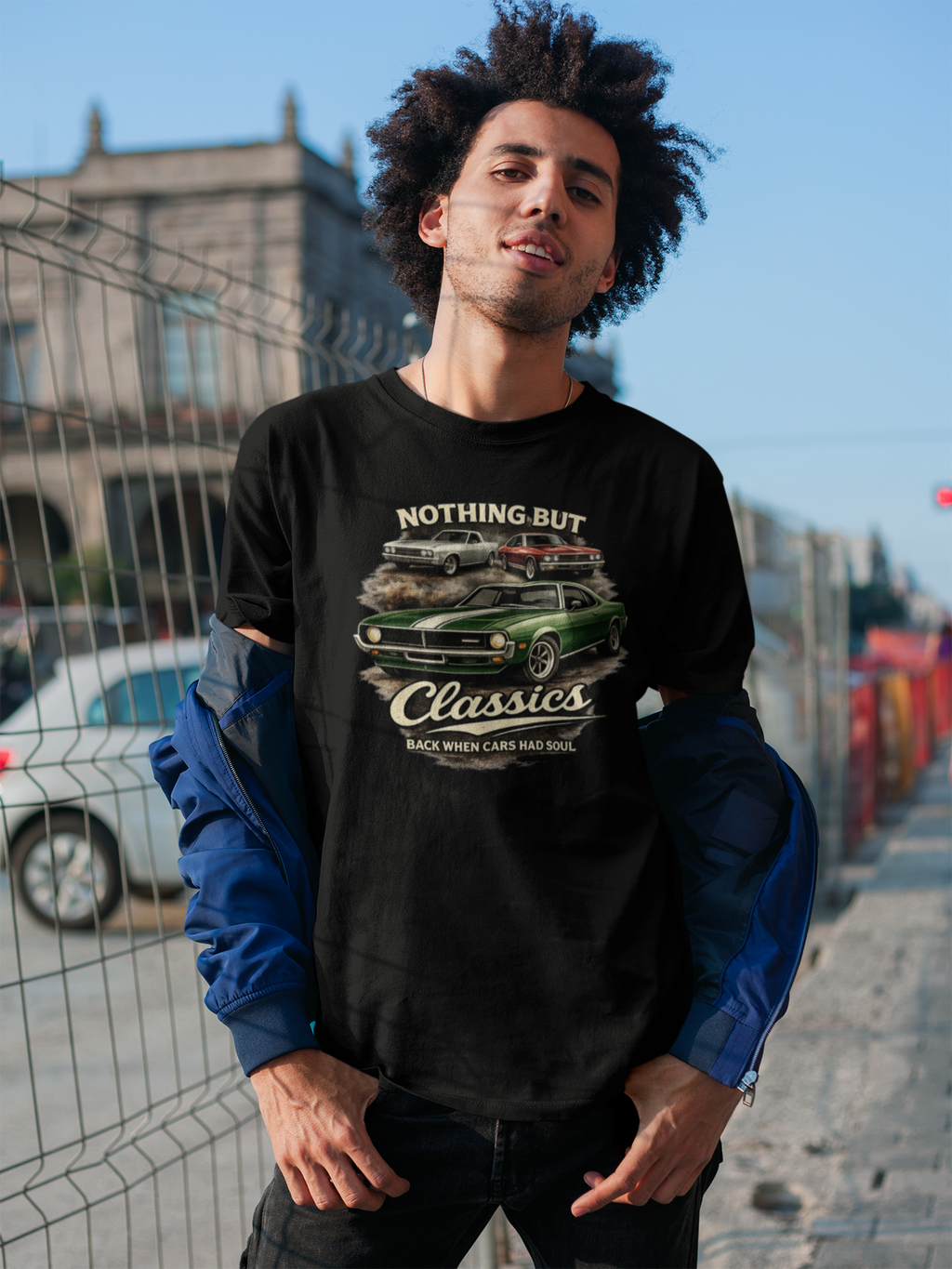 Man wearing a black sweatshirt with a graphic design of a green car and text, standing outdoors.