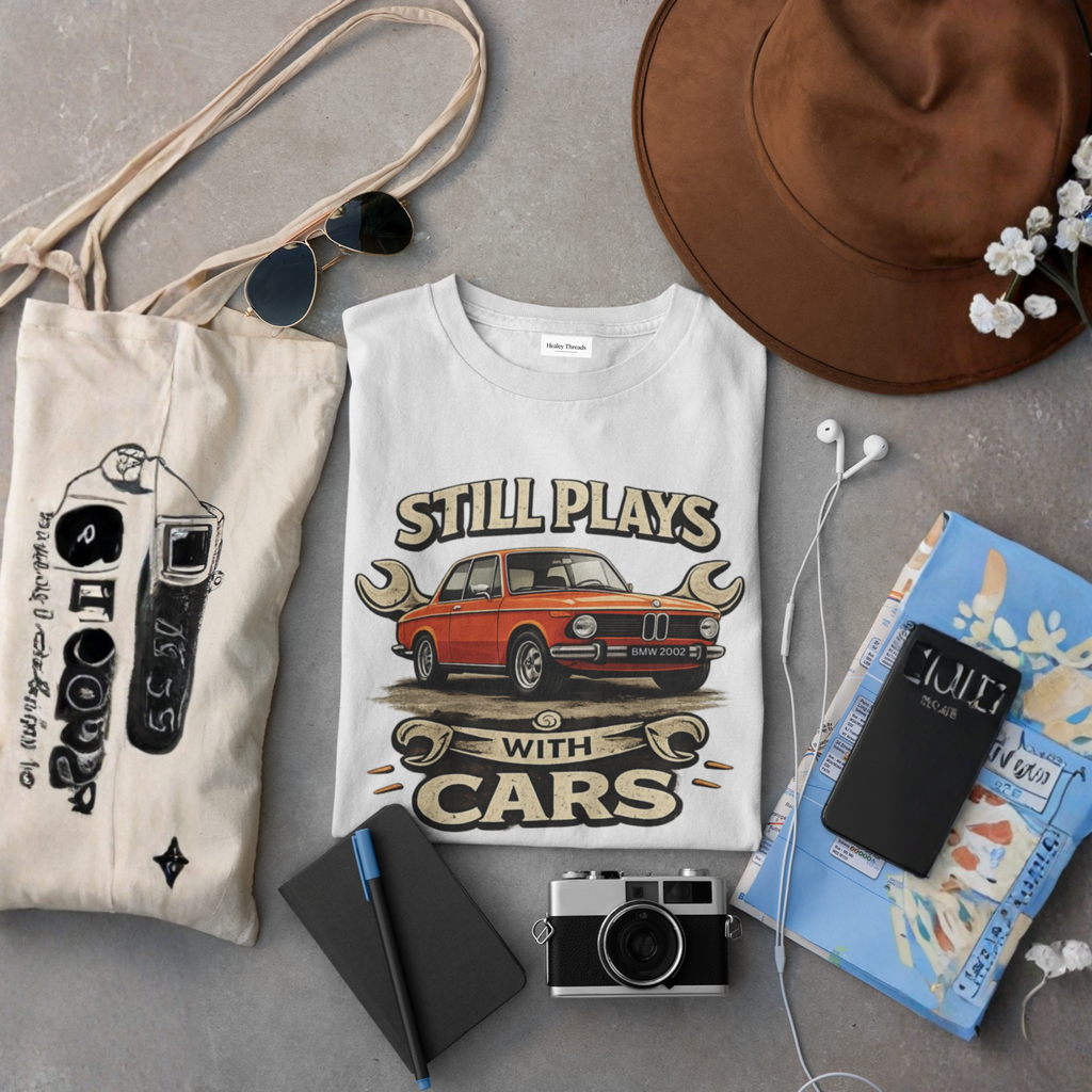 T-shirt with car graphic design, bag, camera, notebook, and hat on a gray surface