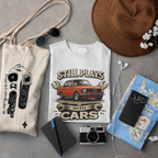 T-shirt with car graphic design, bag, camera, notebook, and hat on a gray surface