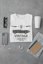 White t-shirt with vintage car design on a gray surface with accessories.