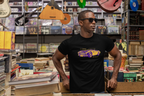 Man wearing a black t-shirt with a graphic design in a store with books and musical instruments.