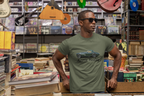 Man wearing a military green t-shirt with a car design in a store with books and musical instruments.