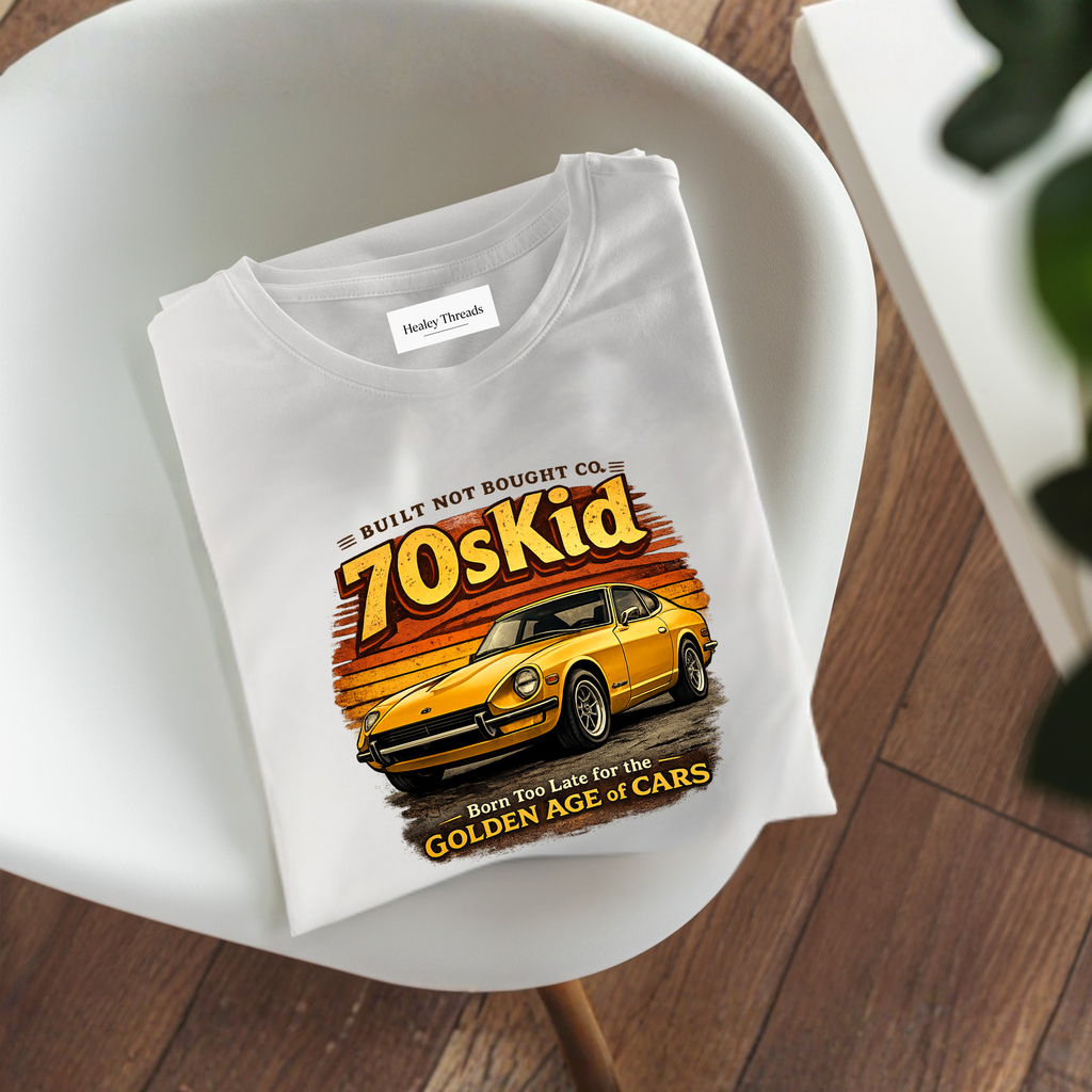 Folded white t-shirt with a vintage yellow car and “70s Kid – Born Too Late for the Golden Age of Cars” design, placed on a modern white chair.