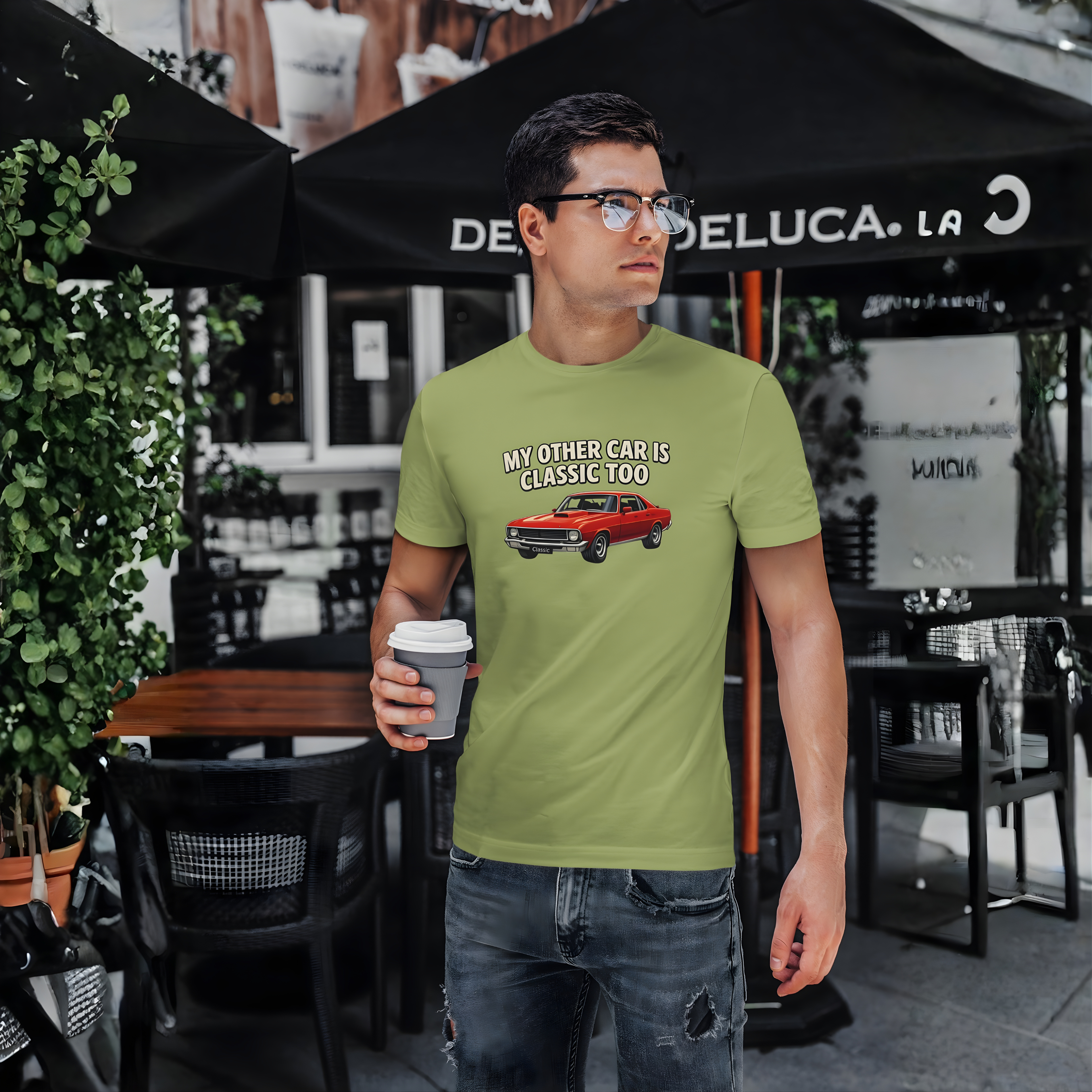 Man wearing a green t-shirt with a graphic and text, standing outdoors under a Deluca restaurant umbrella.
