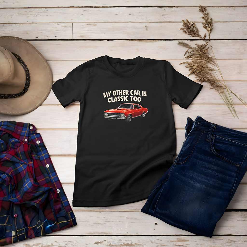 Black t-shirt with red car graphic and text on a wooden surface with jeans, plaid shirt, and hat.