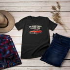 Black t-shirt with red car graphic and text on a wooden surface with jeans, plaid shirt, and hat.