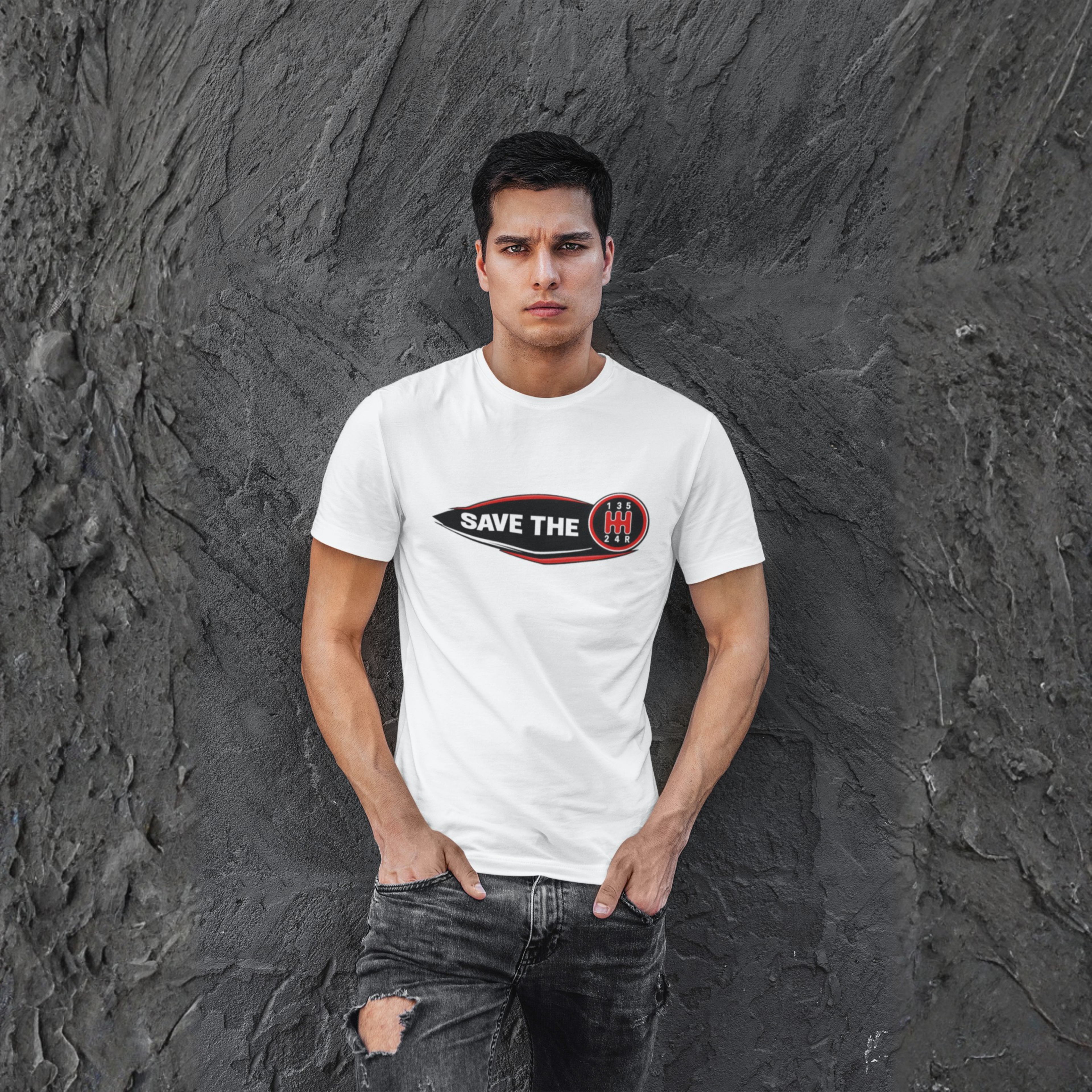 Man wearing a white t-shirt with 'Save the stick shift' graphic design leaning against a grey wall.