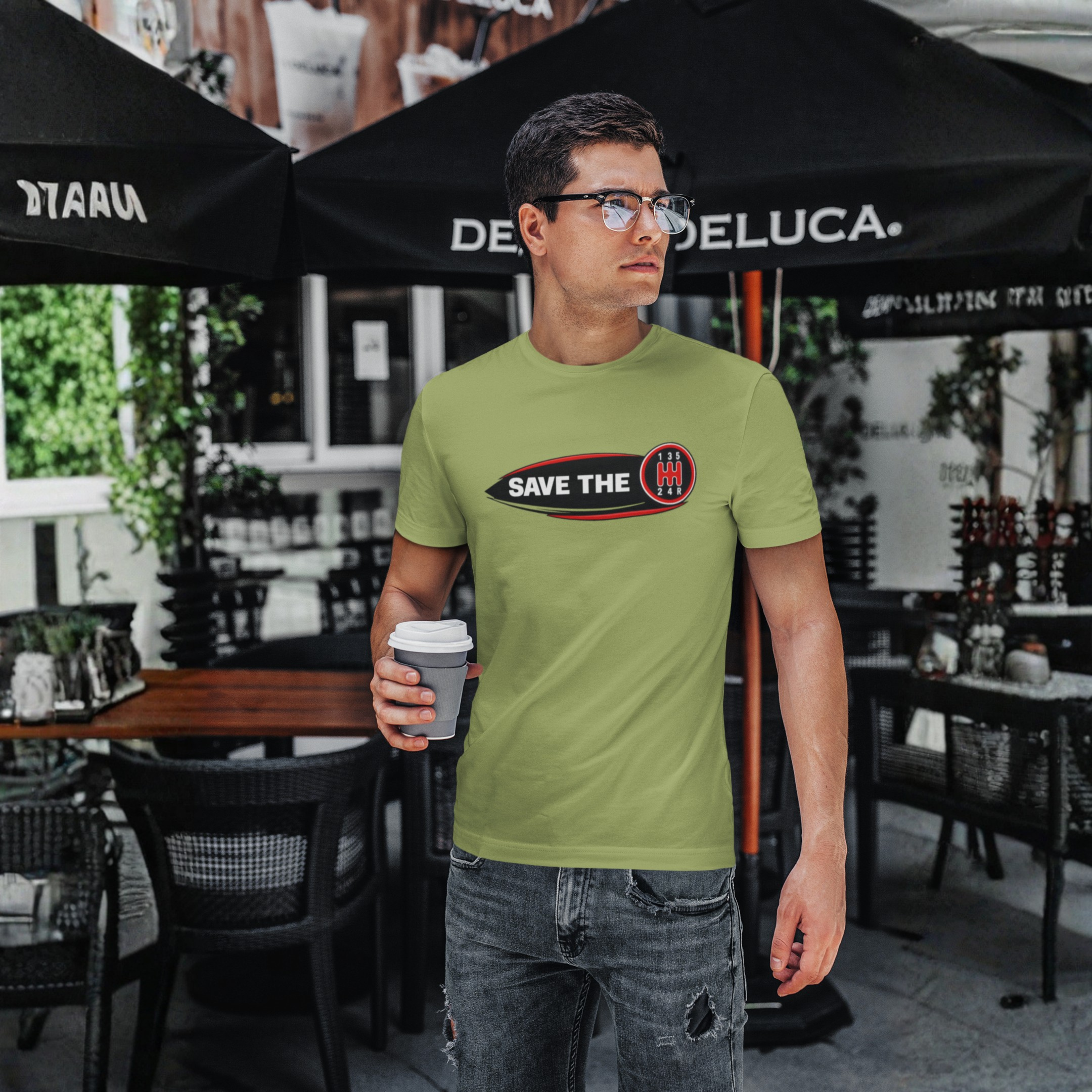 Man wearing a military green t-shirt with 'Save the stick shift' graphic design holding a cup of coffee.