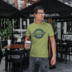 Man wearing a military green t-shirt with 'Heritage Classic Collection' design, holding a coffee cup outdoors.