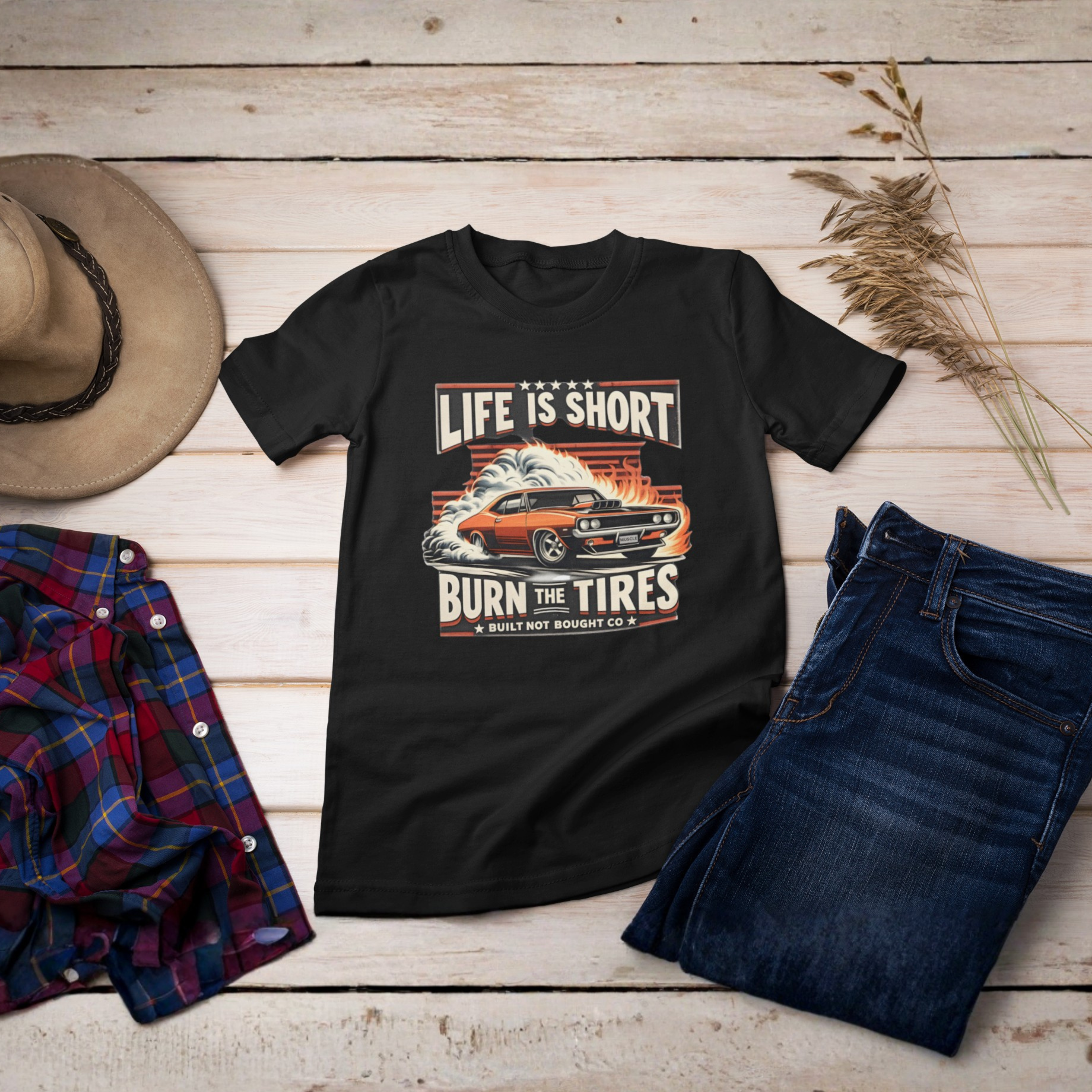 Black t-shirt with graphic design on a wooden surface with jeans, plaid shirt, and hat.