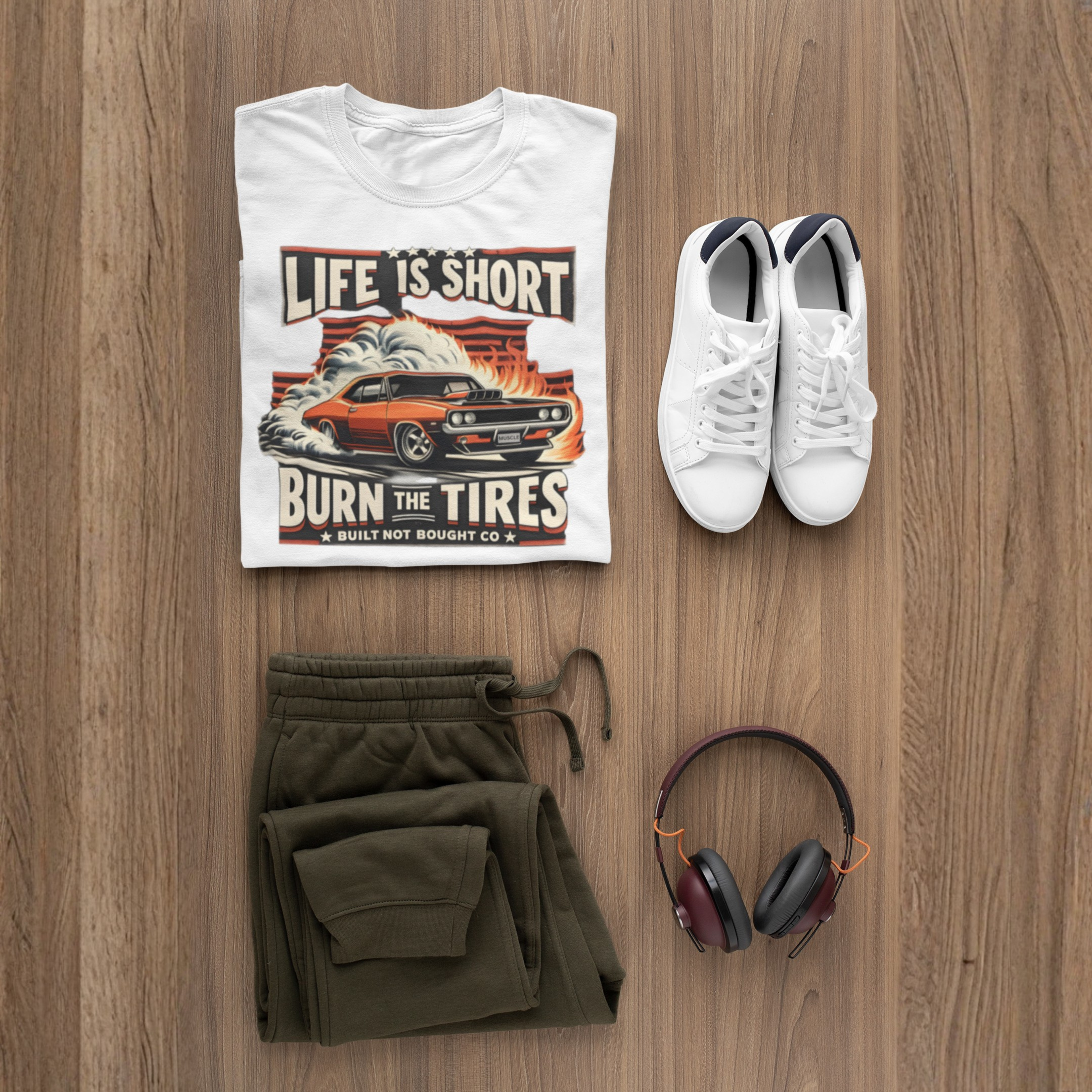 White t-shirt with graphic design, green pants, white sneakers, and headphones on a wooden surface