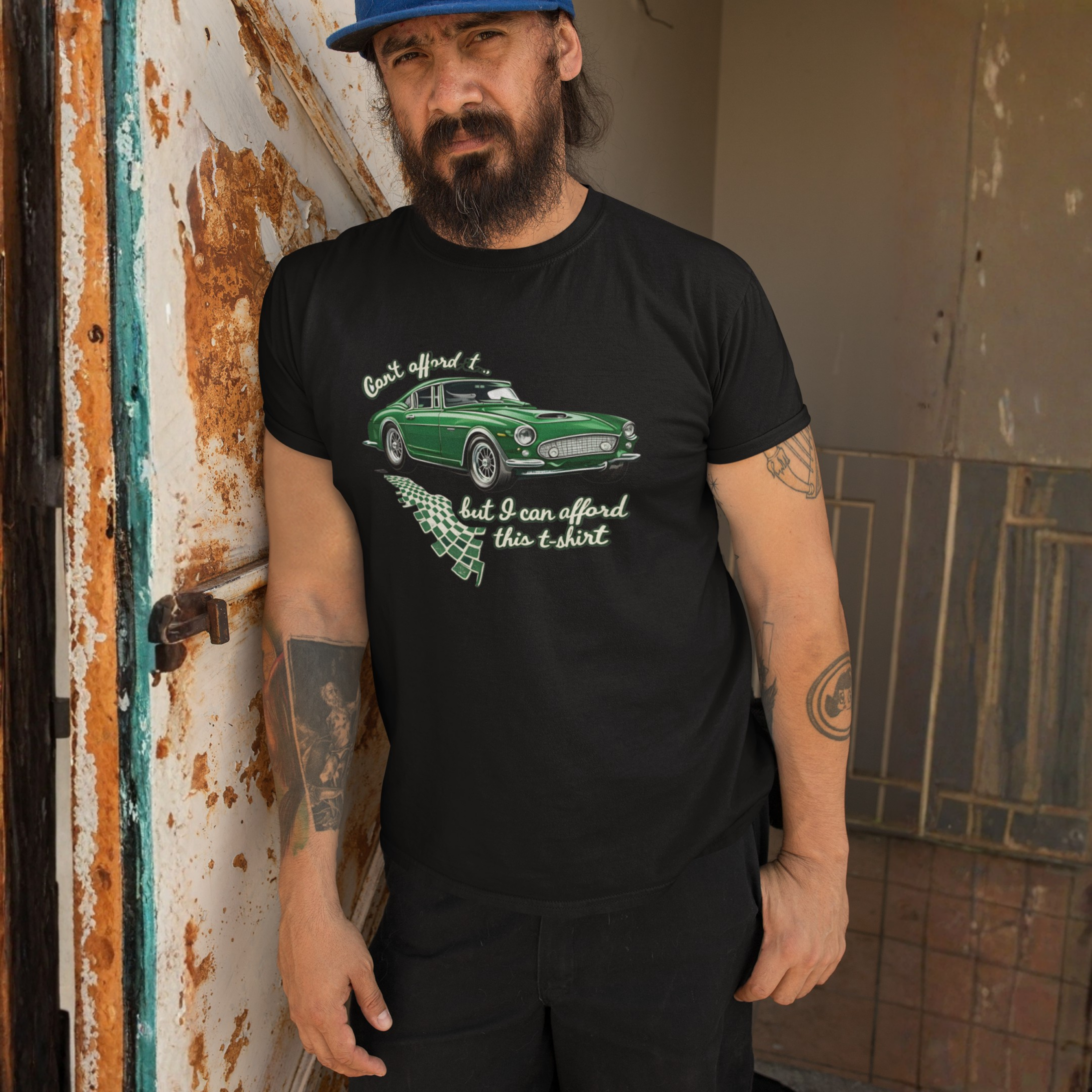 Man wearing a black t-shirt with a green car graphic and text, standing against a rusty metal wall.