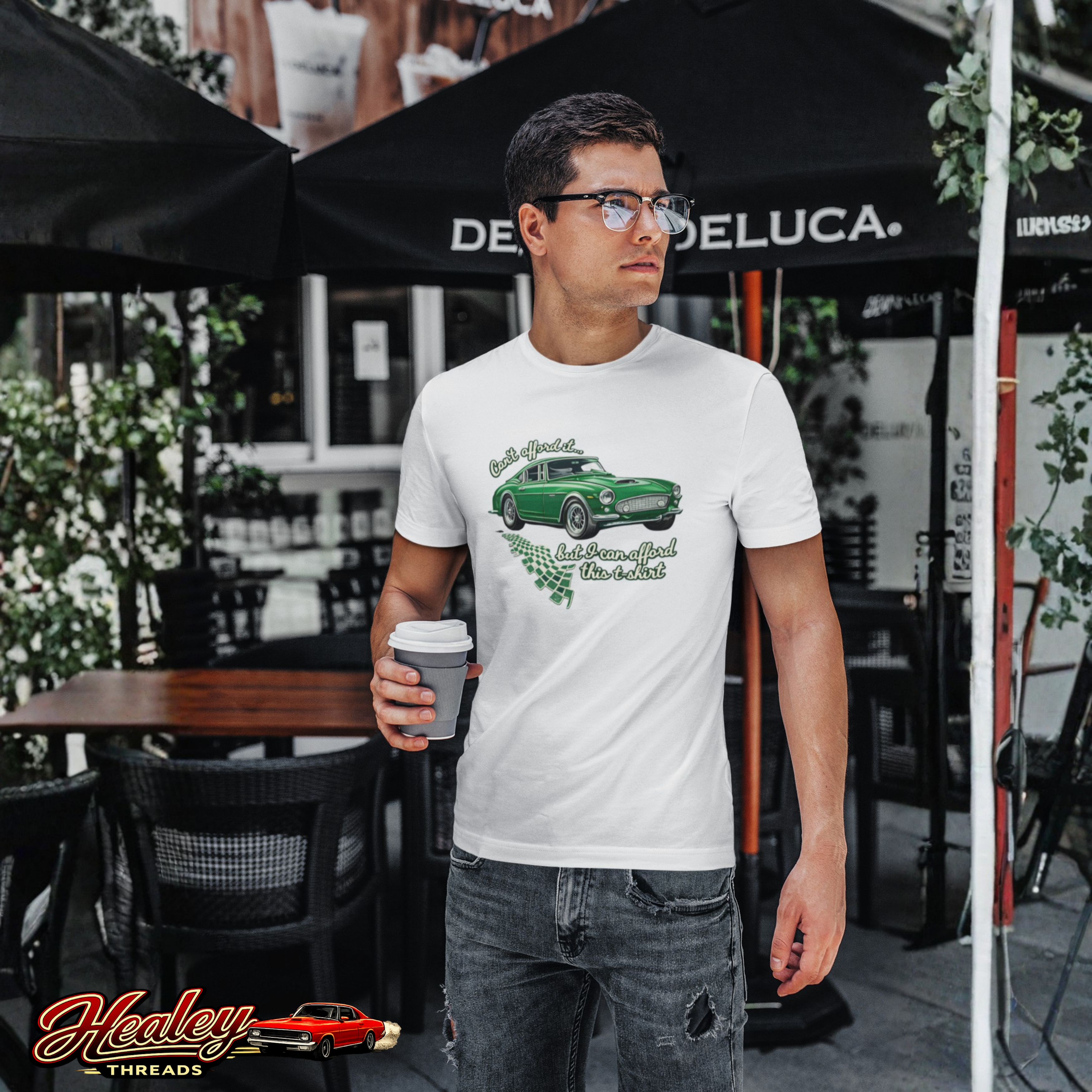 Man wearing a white t-shirt with a green car graphic, standing outdoors under a Deluca umbrella.