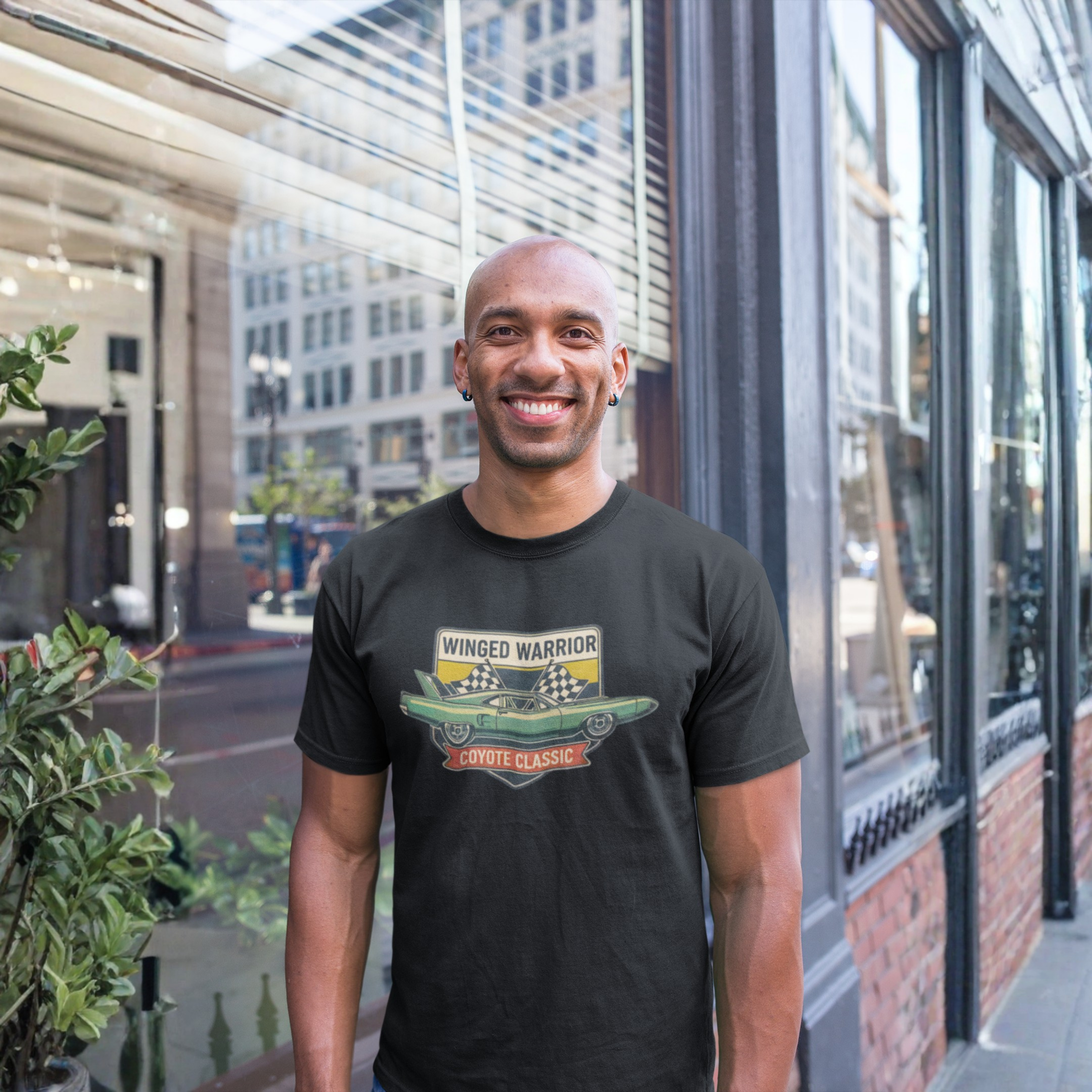 Man wearing a black t-shirt with a graphic design standing in front of a glass building.