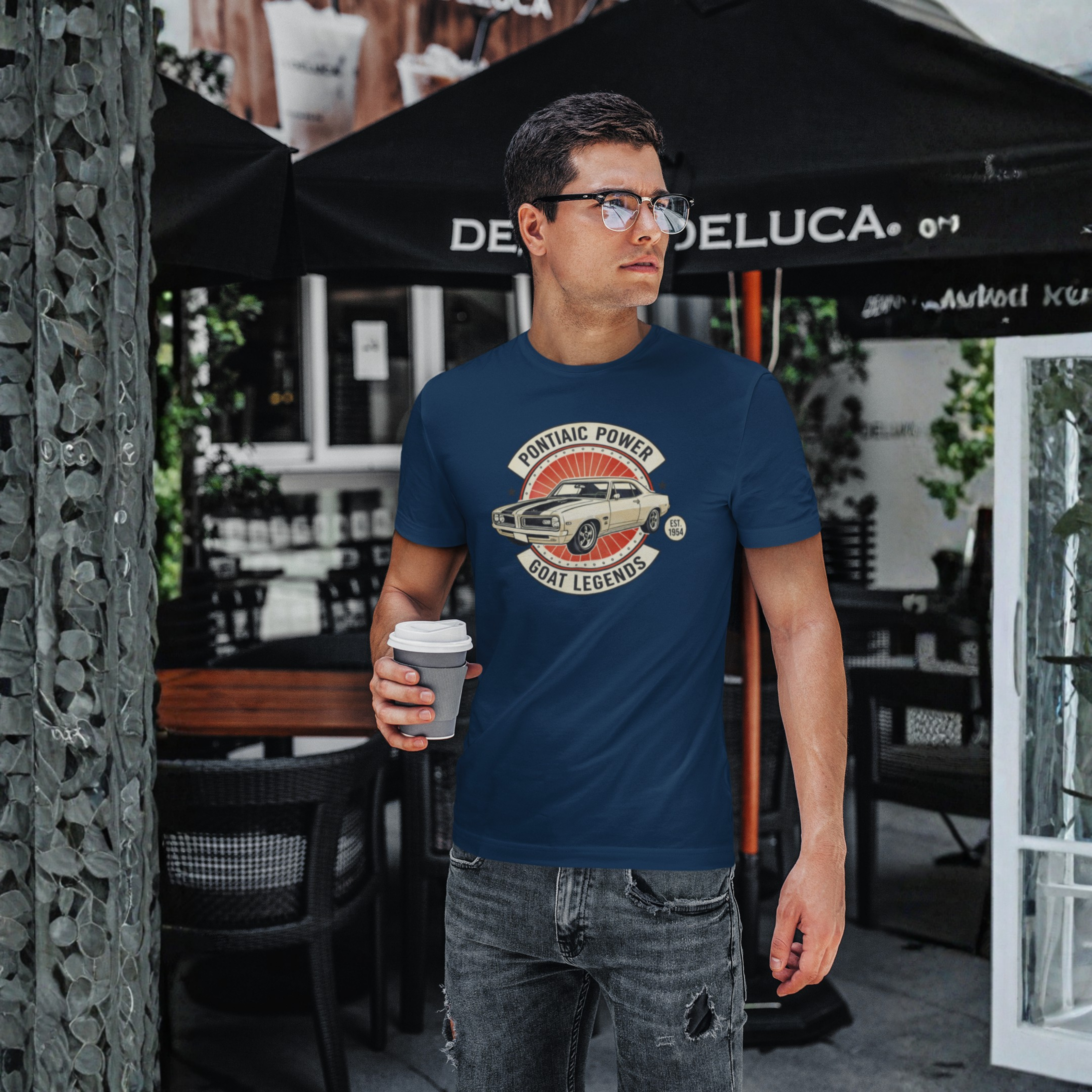 Man wearing a blue t-shirt with a graphic design, holding a coffee cup, standing outdoors.