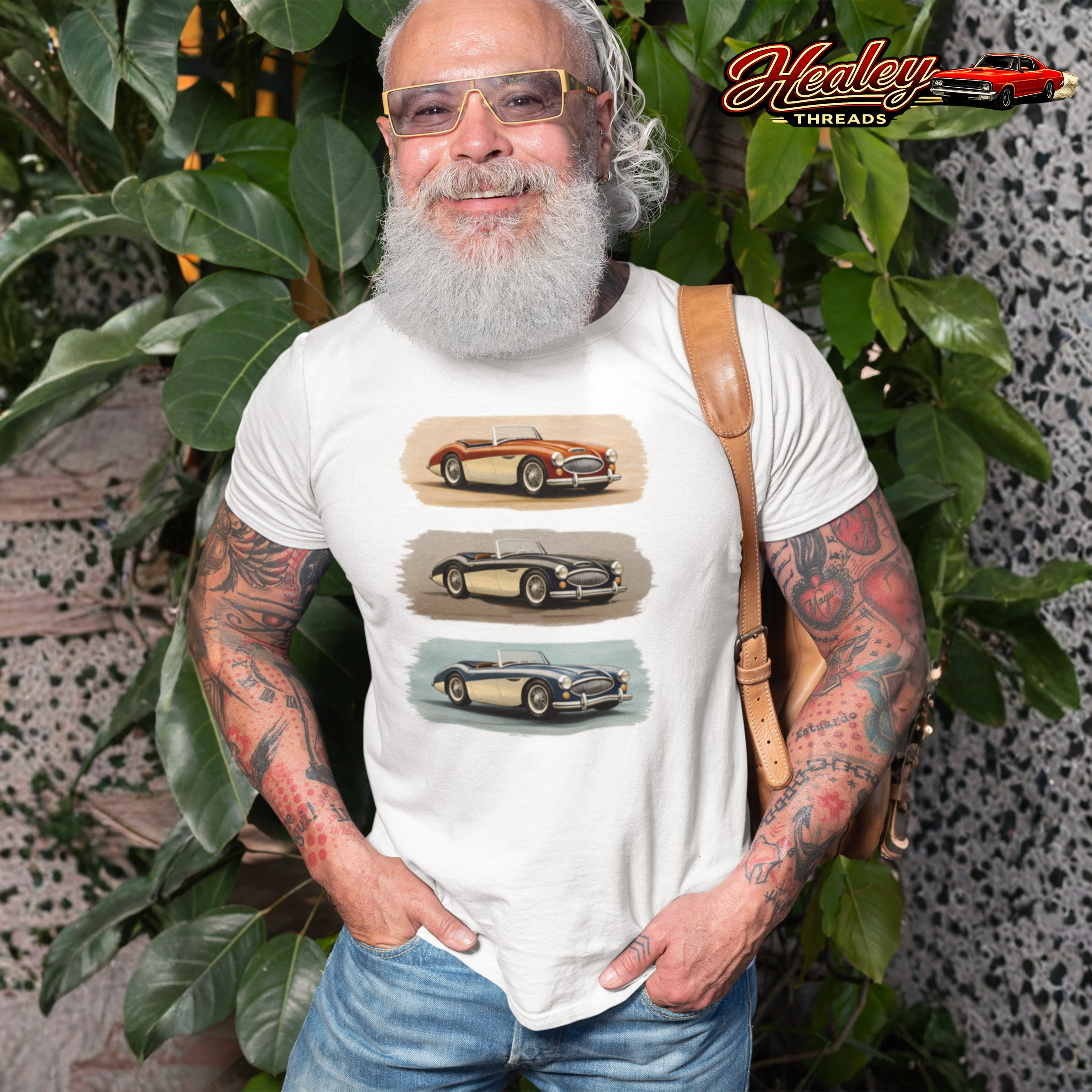 Man wearing a white Healey  t-shirt with vintage car graphics, standing outdoors with greenery.