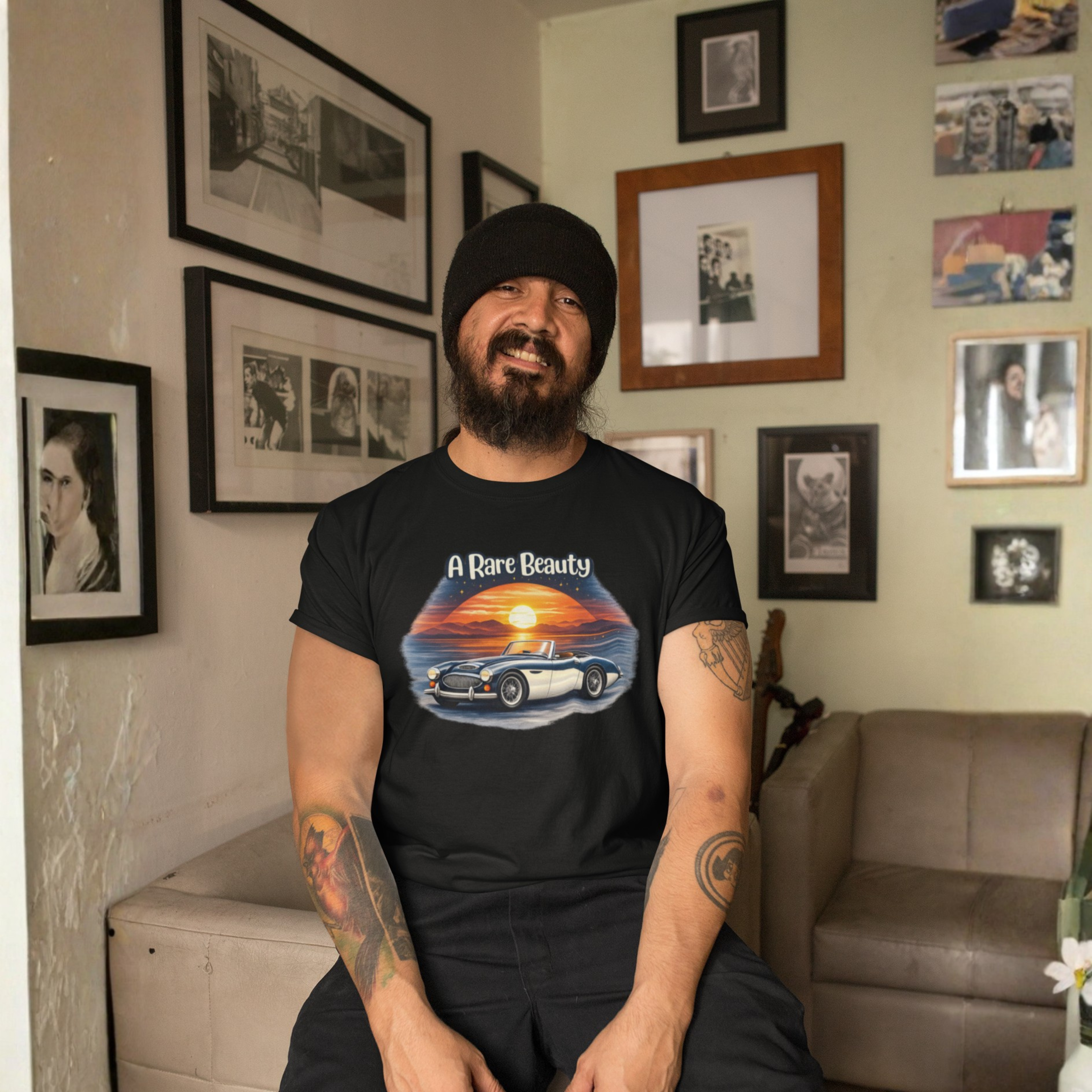 Man wearing a black t-shirt with a graphic design of a sunset and car, sitting in a room with framed pictures on the wall.