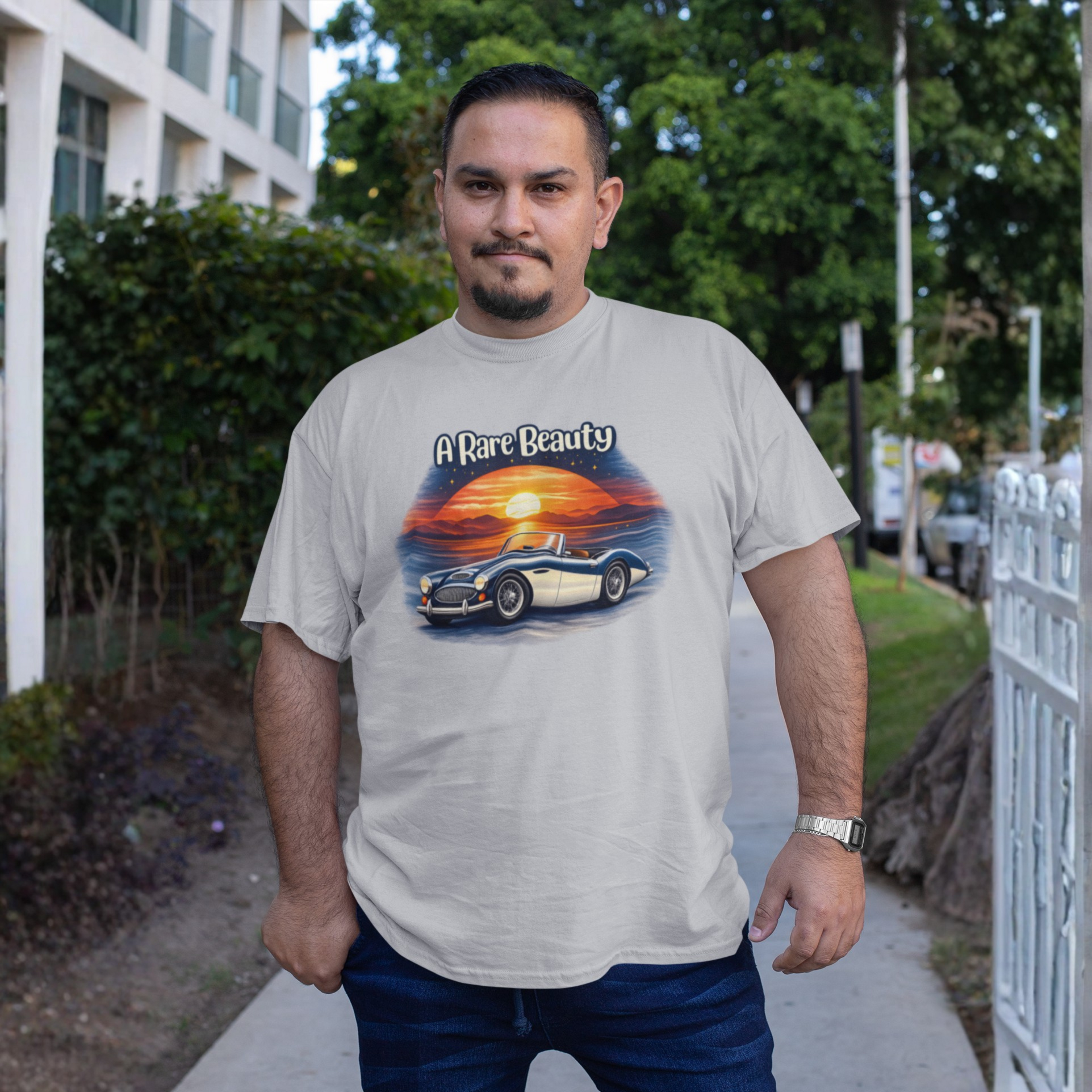 Man wearing ash t-shirt with a graphic of a classic car and sunset, labeled 'A Rare Beauty', on a street background.