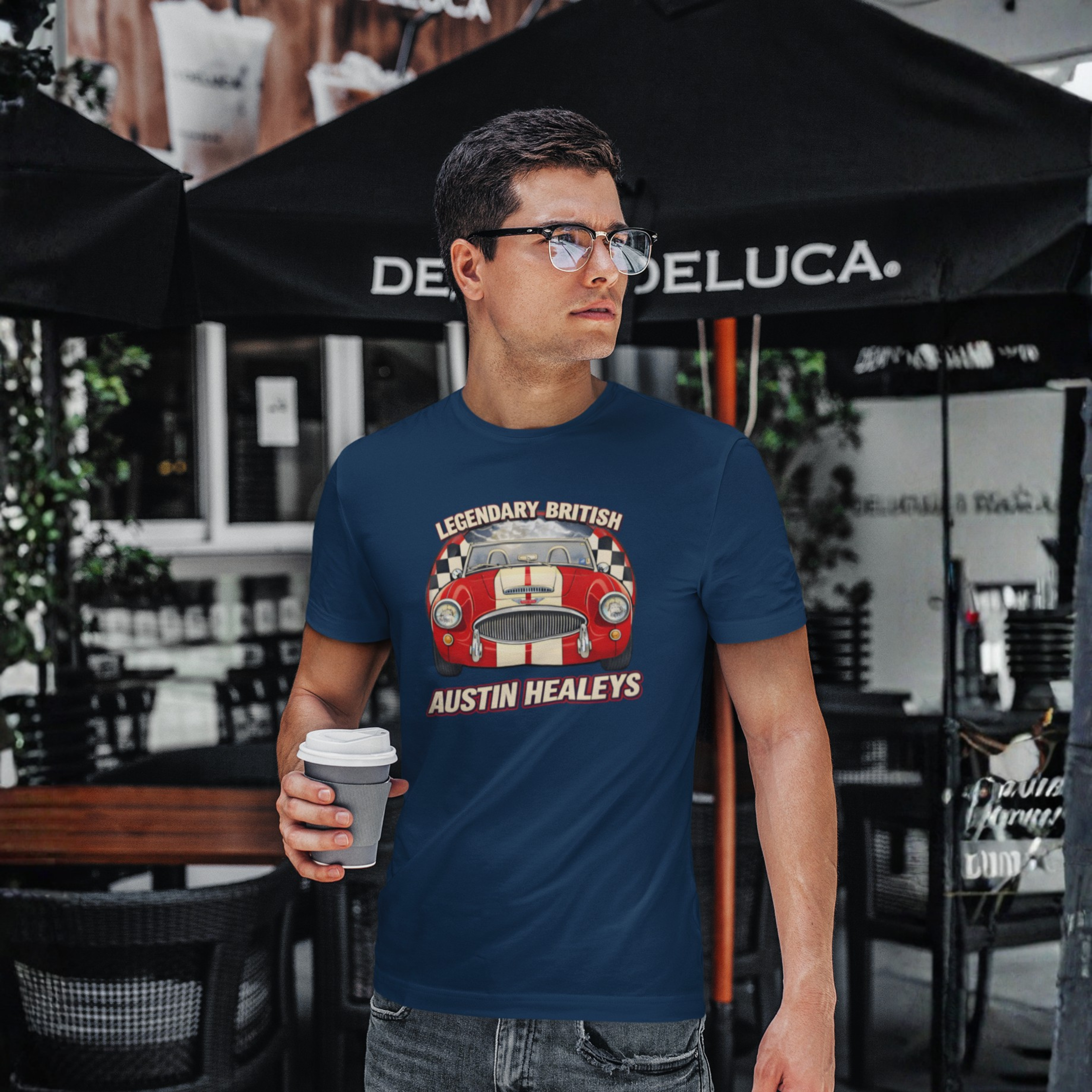 Man wearing a navy blue t-shirt with an Austin Healey design, holding a coffee cup outdoors.