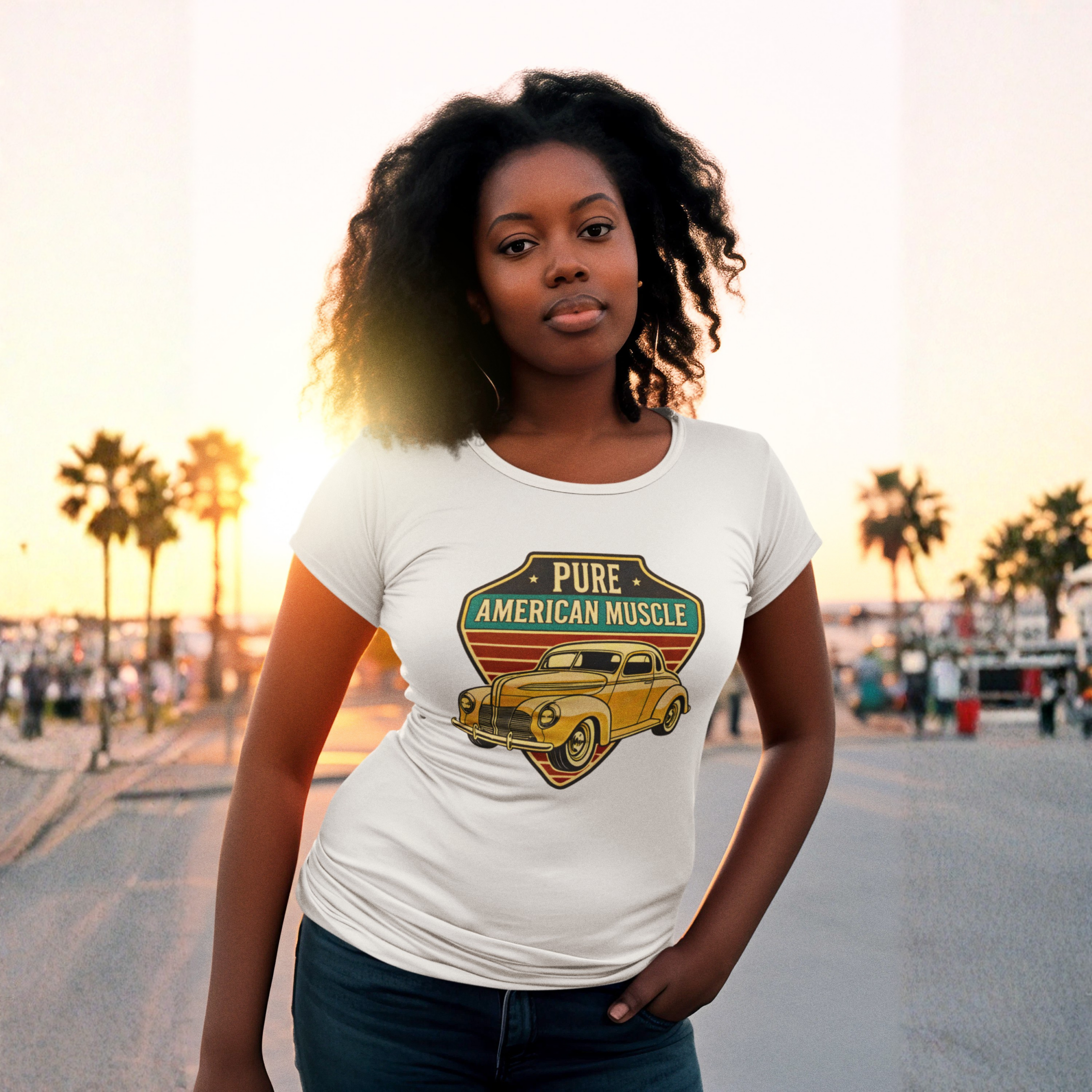 Woman wearing a white t-shirt with a graphic design of a vintage car and text, standing on a street with palm trees in the background.
