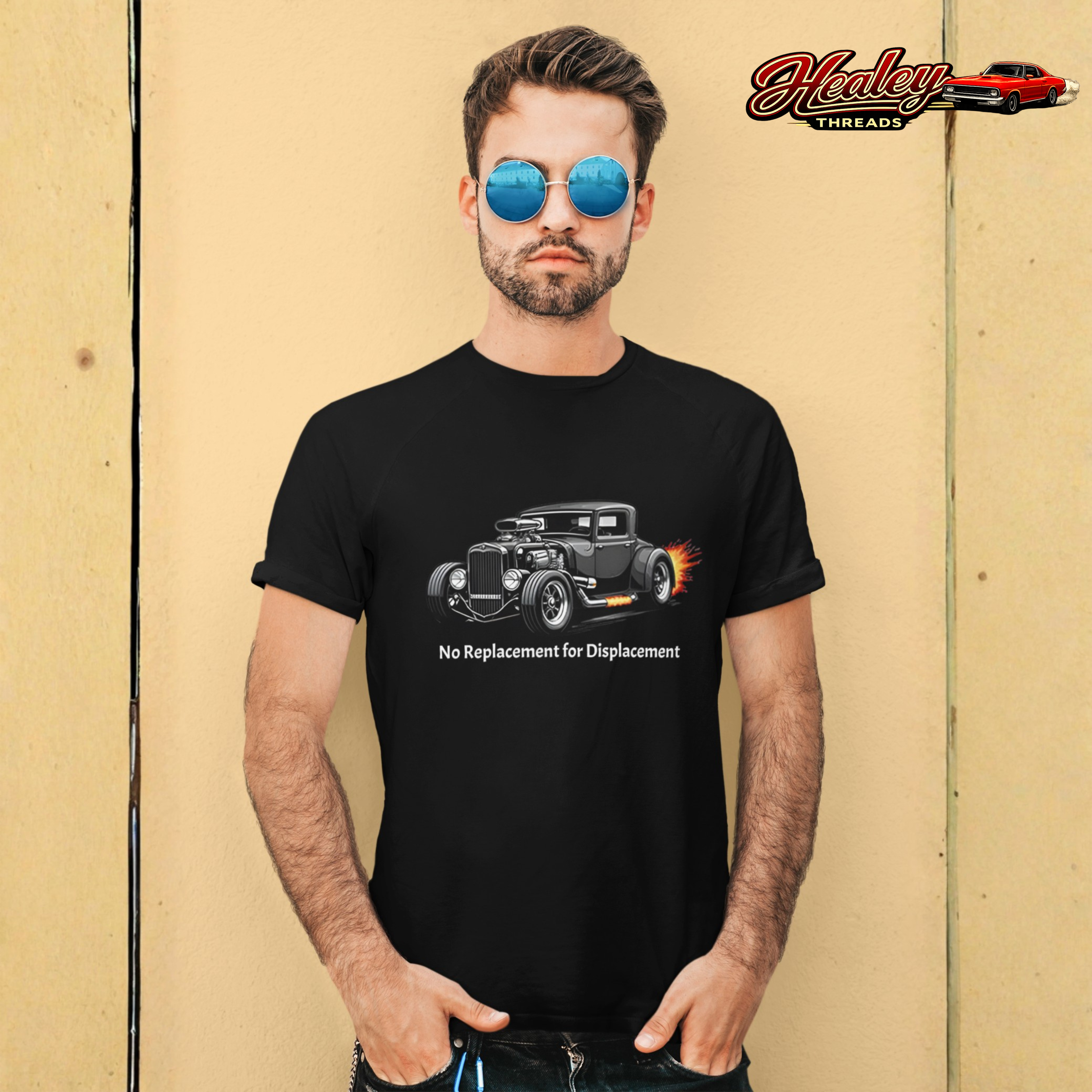 Man wearing a black t-shirt with a hot rod graphic and text, standing against a beige wall with 'Healey Threads' logo.