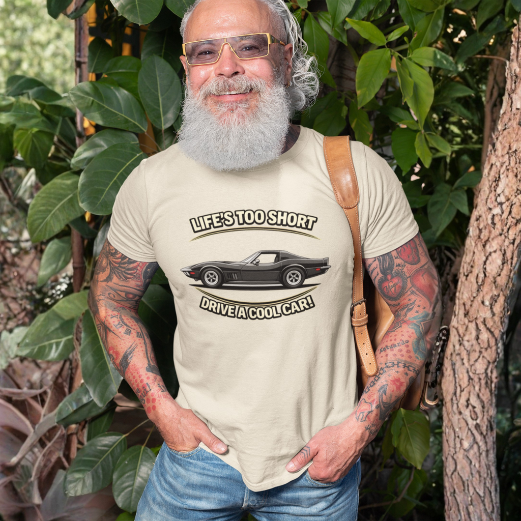 Man wearing a sand t-shirt with a vintage vette graphic and text, standing outdoors among greenery.