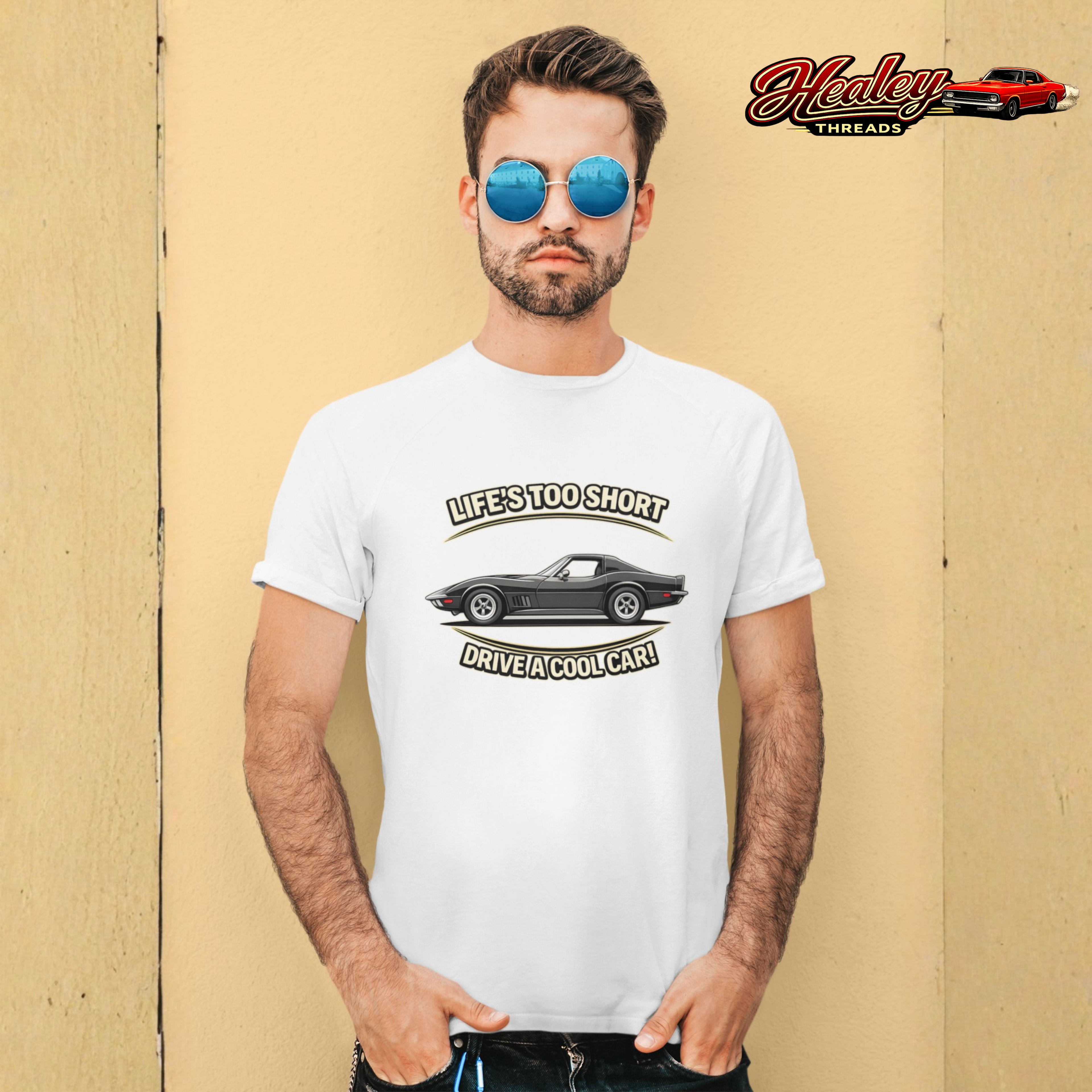 Man wearing a white t-shirt with a graphic vintage vette design and sunglasses, standing against a beige wall.