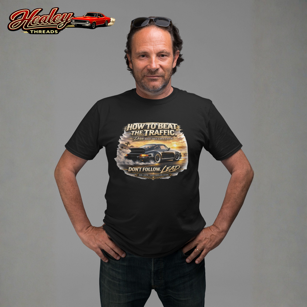 Man wearing a black t-shirt with a classic car graphic design and text, standing against a gray background. Healey Threads logo is visible.