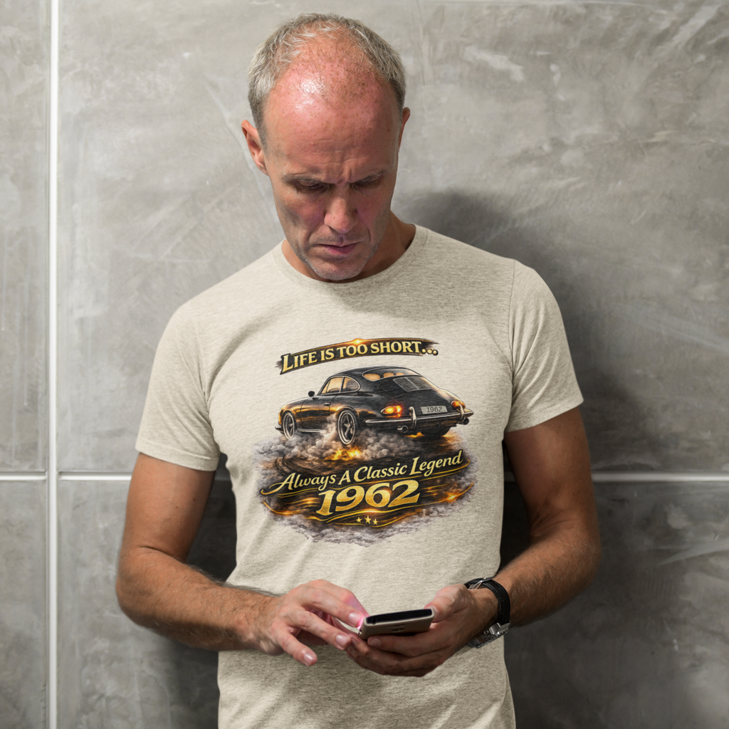 Man wearing a sand t-shirt with a classic car graphic design and text, standing against a gray wall.