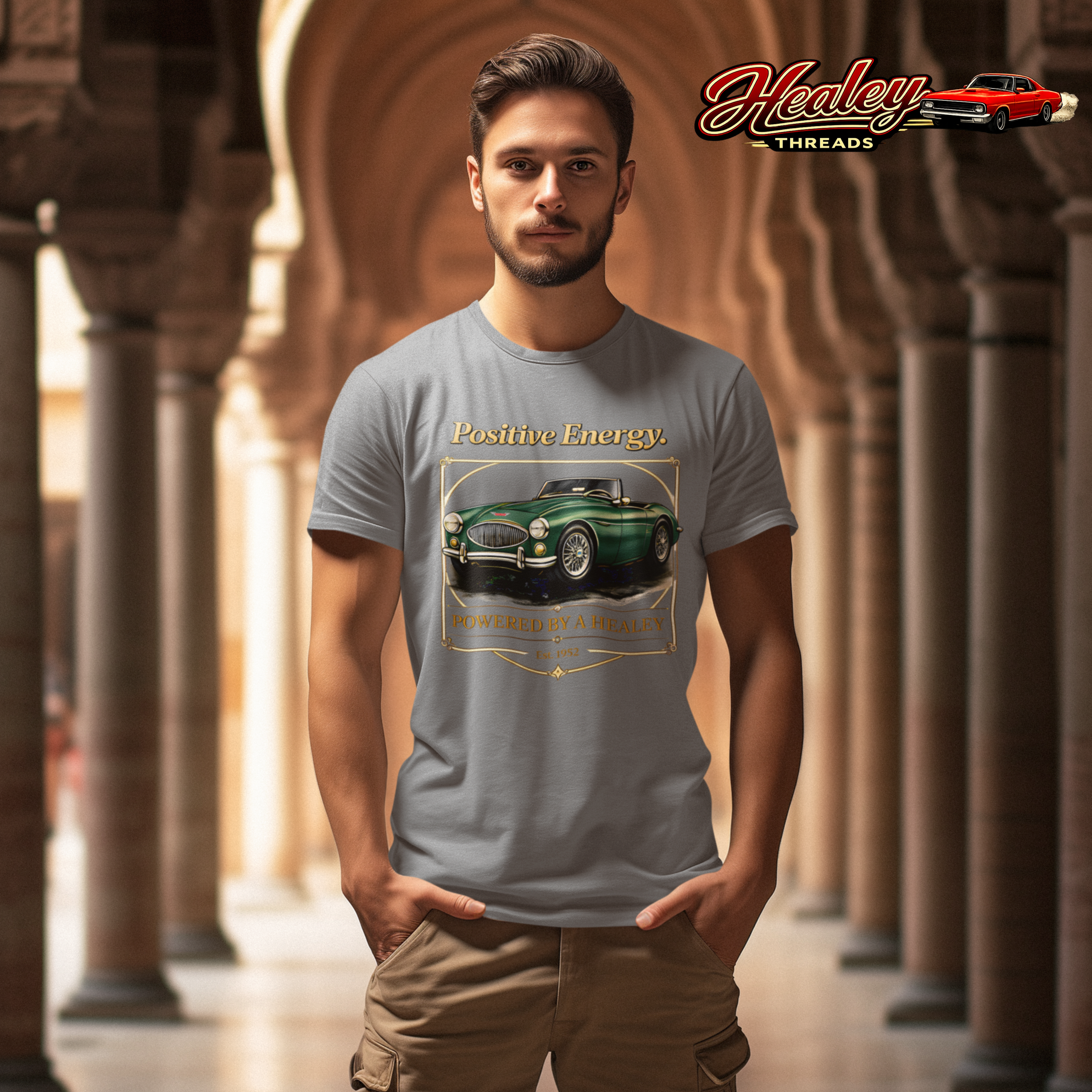 Man wearing a gray t-shirt with a green classic car graphic and 'Positive Energy' text, standing in an arched hallway.