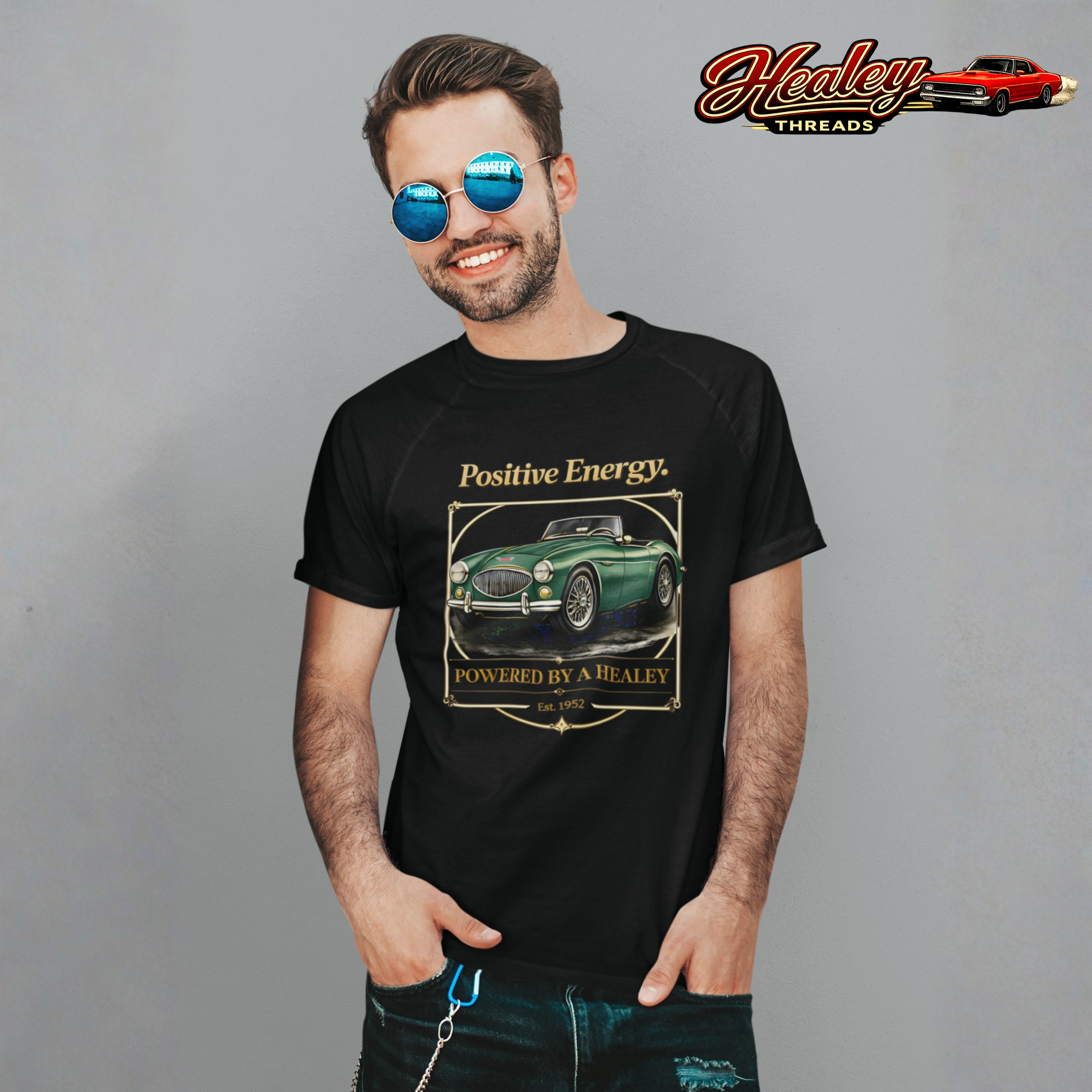 Man wearing a black t-shirt with a classic car graphic and text, standing against a gray background with 'Healey Threads' logo.